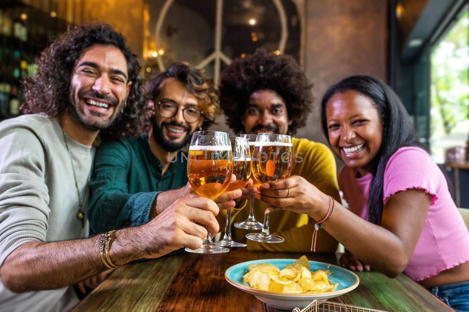 Happy multiracial friends in a bar looking at camera toasting with beer. Lifestyle concept.