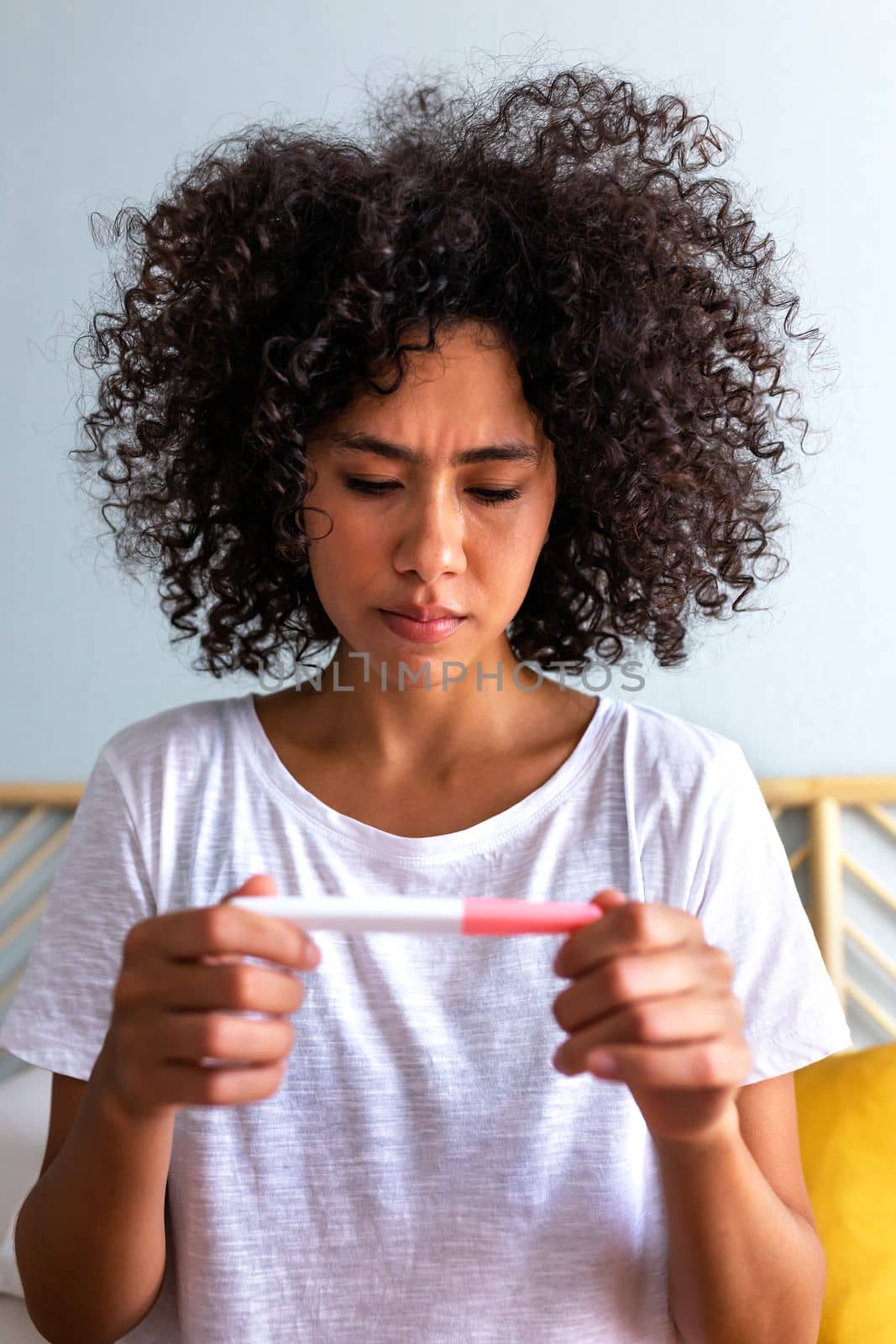 Woman sad to see negative pregnancy test. Young African American woman worried after checking pregnancy test. Vertical. by Hoverstock