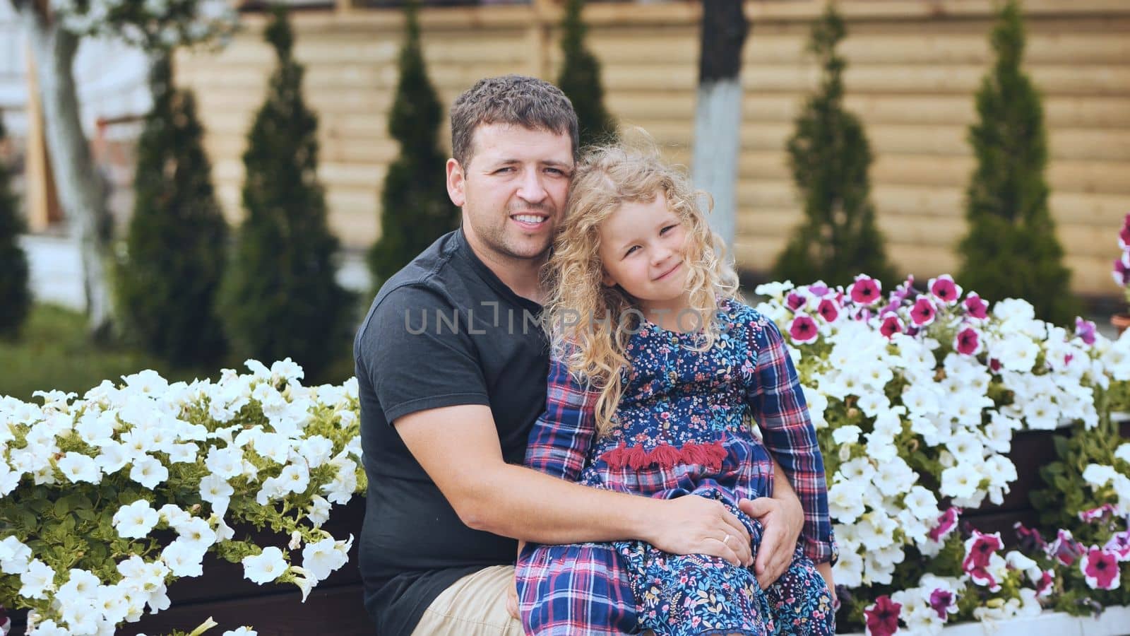 A portrait of a father with his young daughter in the garden against a background of white petunias