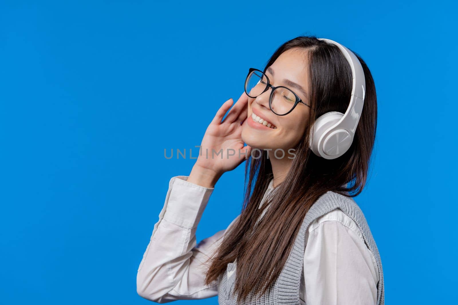 Happy student teenager listening music, enjoying dance with headphones on blue studio backdrop. Radio, wireless modern sound technology, online player. Copy space. High quality photo