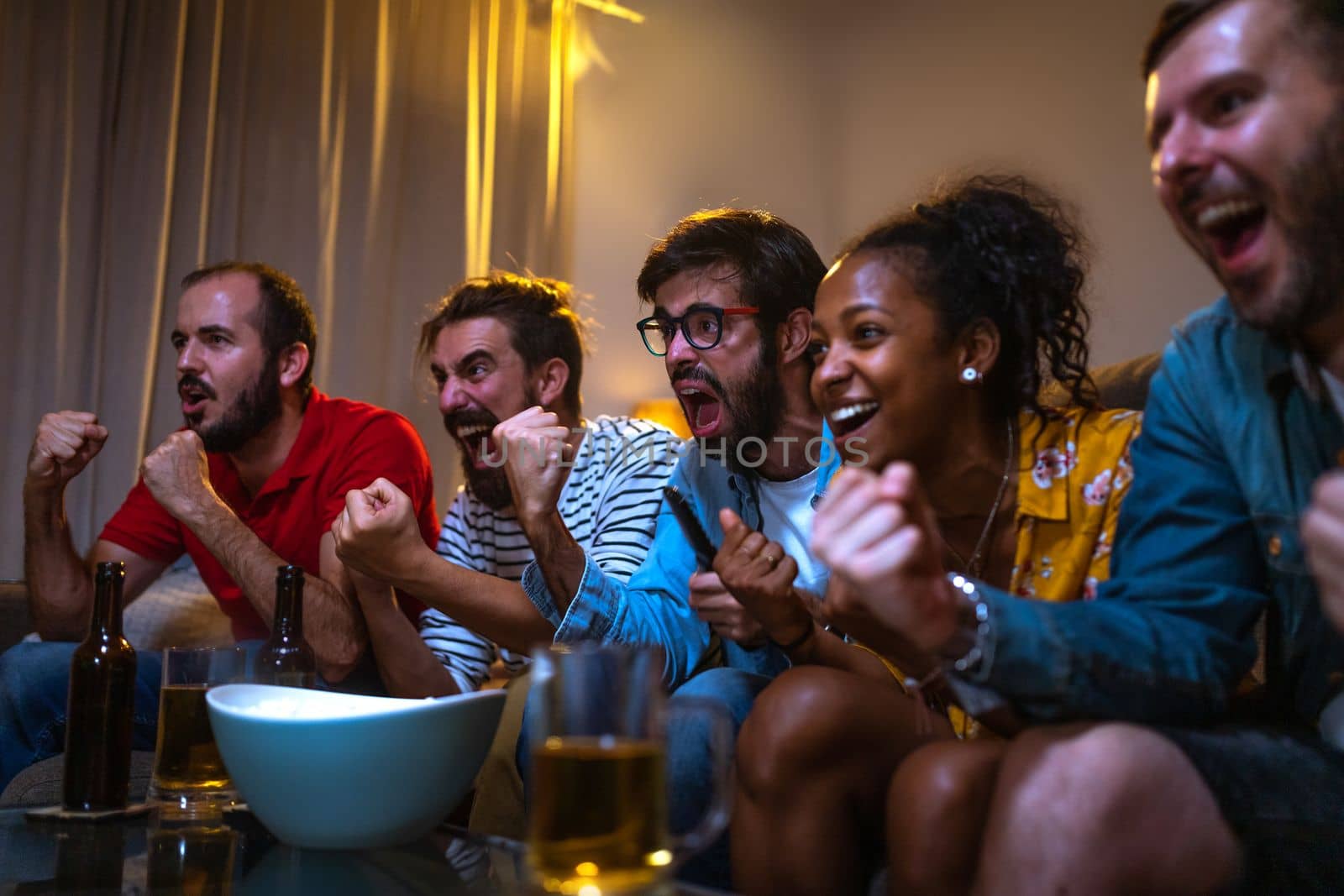 Group of friends watching football game on tv celebrating team victory. Soccer fans celebrating team scoring goal. Leisure activities concept.