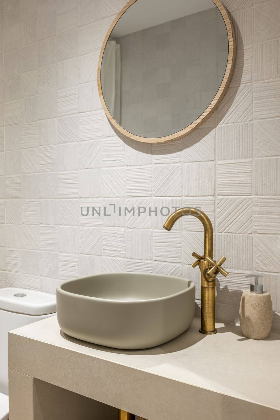 Neat stylish oval-shaped sink on white marble countertop with an elegant copper-coloured faucet. Above sink hangs a round modern gold-framed mirror