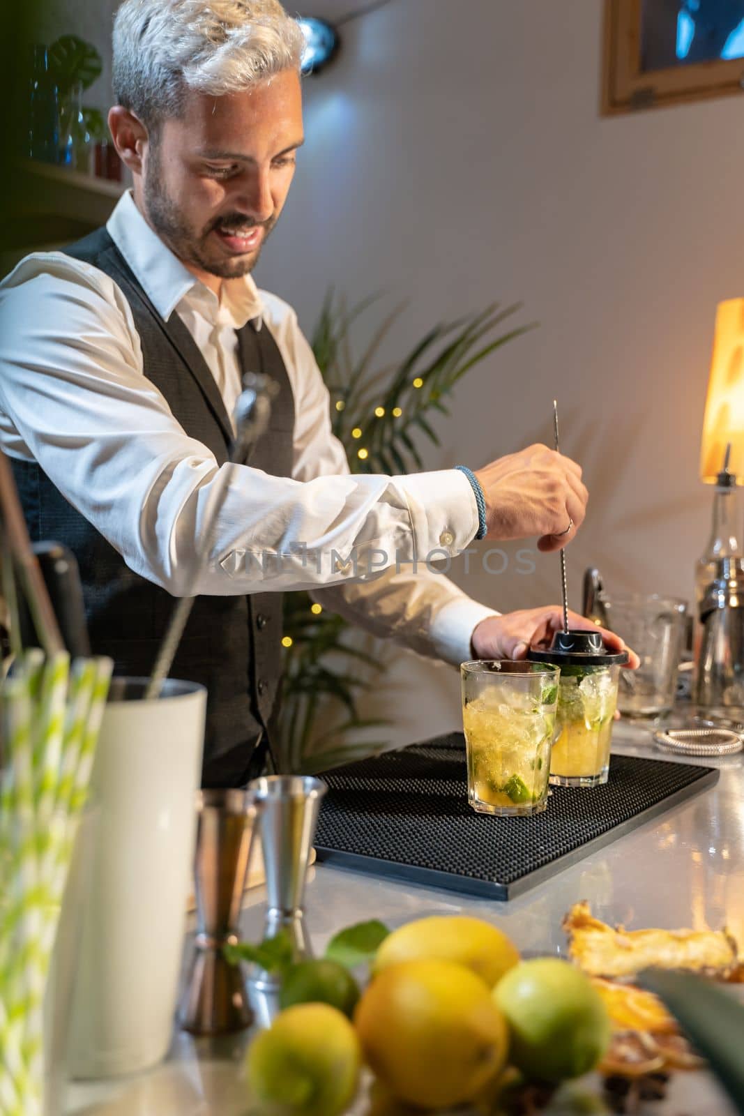 Barman making cocktail Mojito in night club adding ingredients and creating expert drinks on bar counter. High quality vertical photo