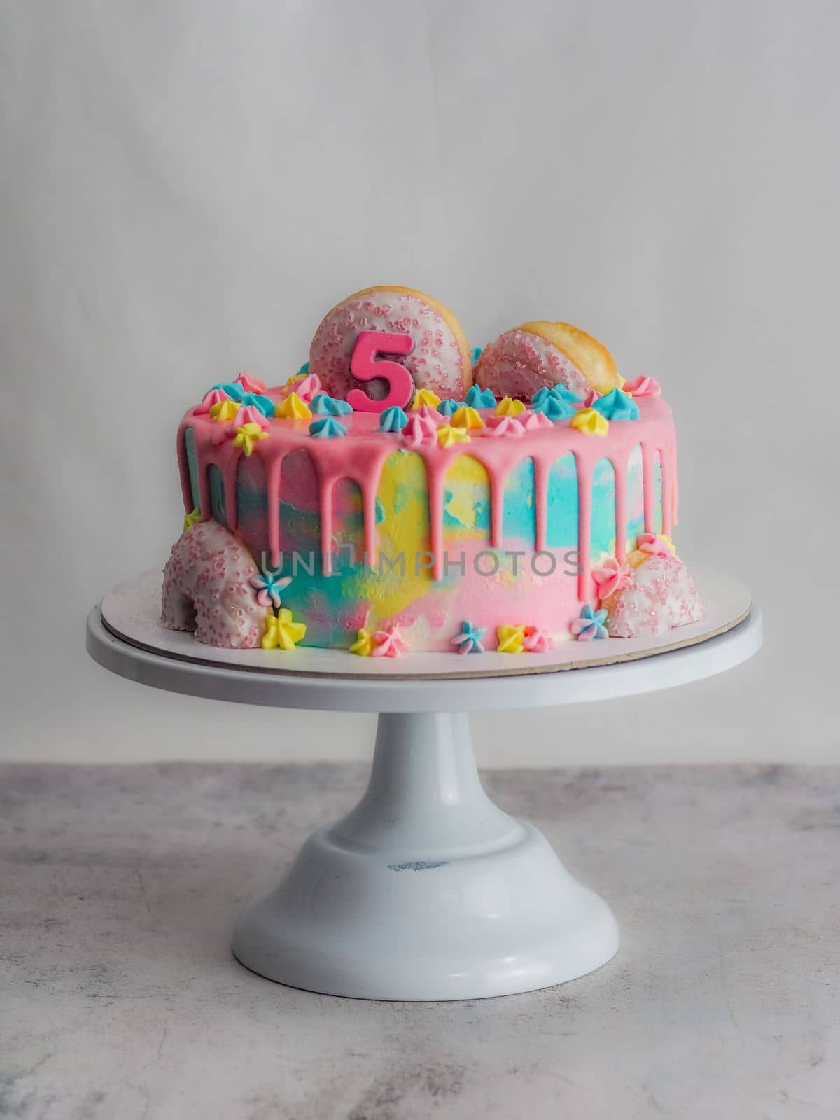 Close up of pink frosted dripping cake with donut and plastel brushed royal star sprinkles insolated on white studio shot