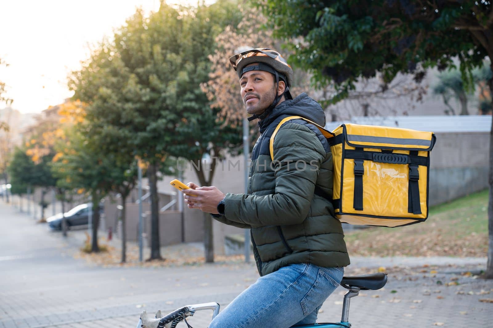 Food delivery concept. Young black man driver with backpack looking smartphone in the city by PaulCarr