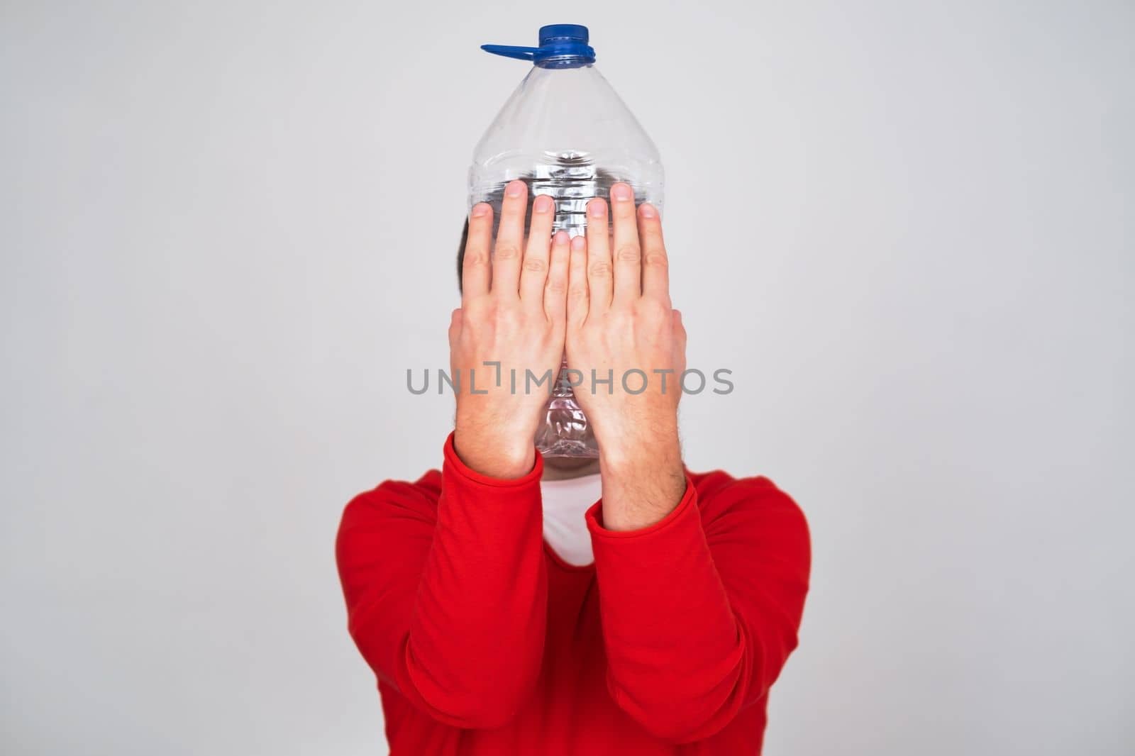 Recycle waste management concept. Caucasian man hiding behind an empty water bottle.