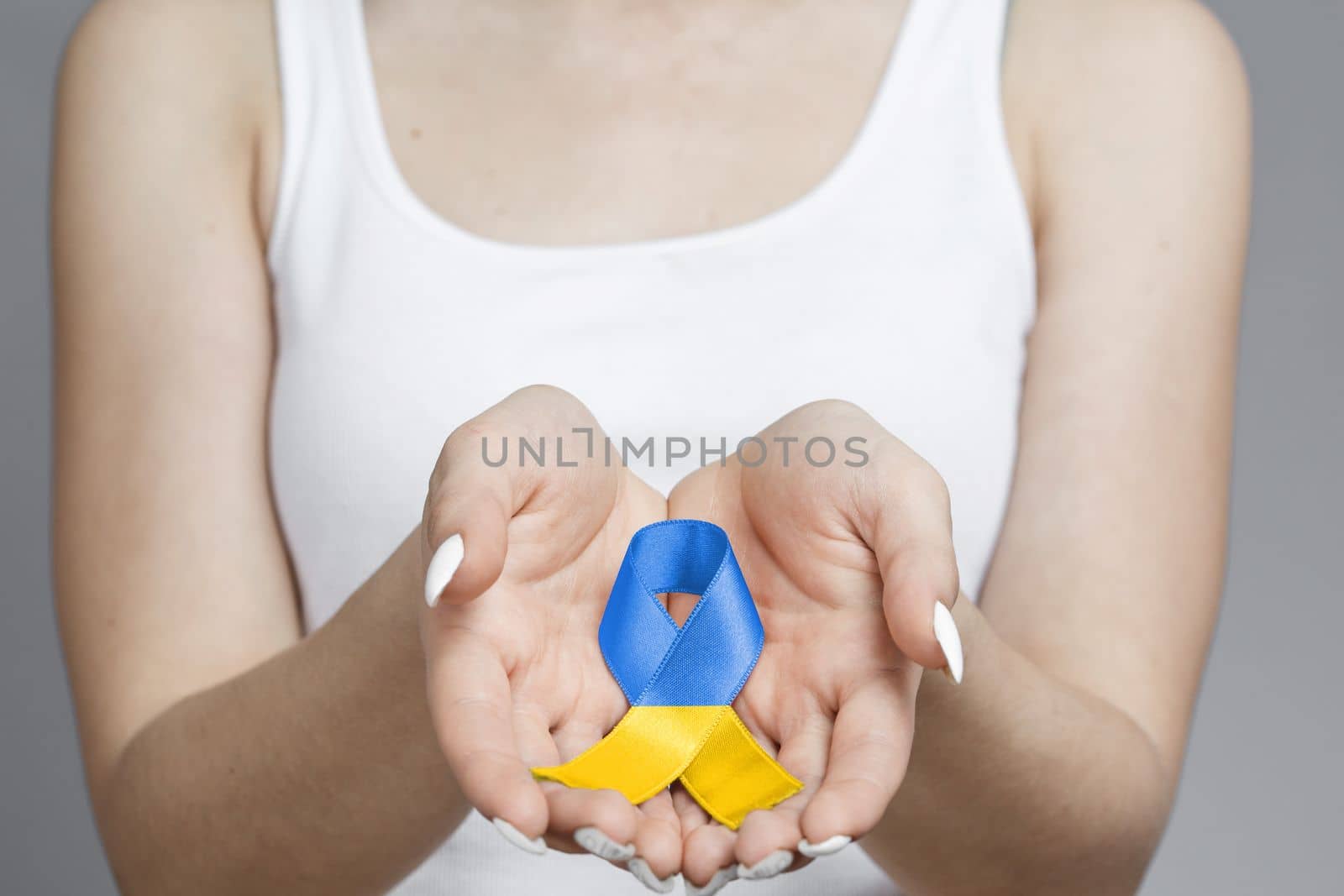 blue and yellow ukrainian ribbon lies in palms of women in white T shirt. concept needs help and support, truth will win