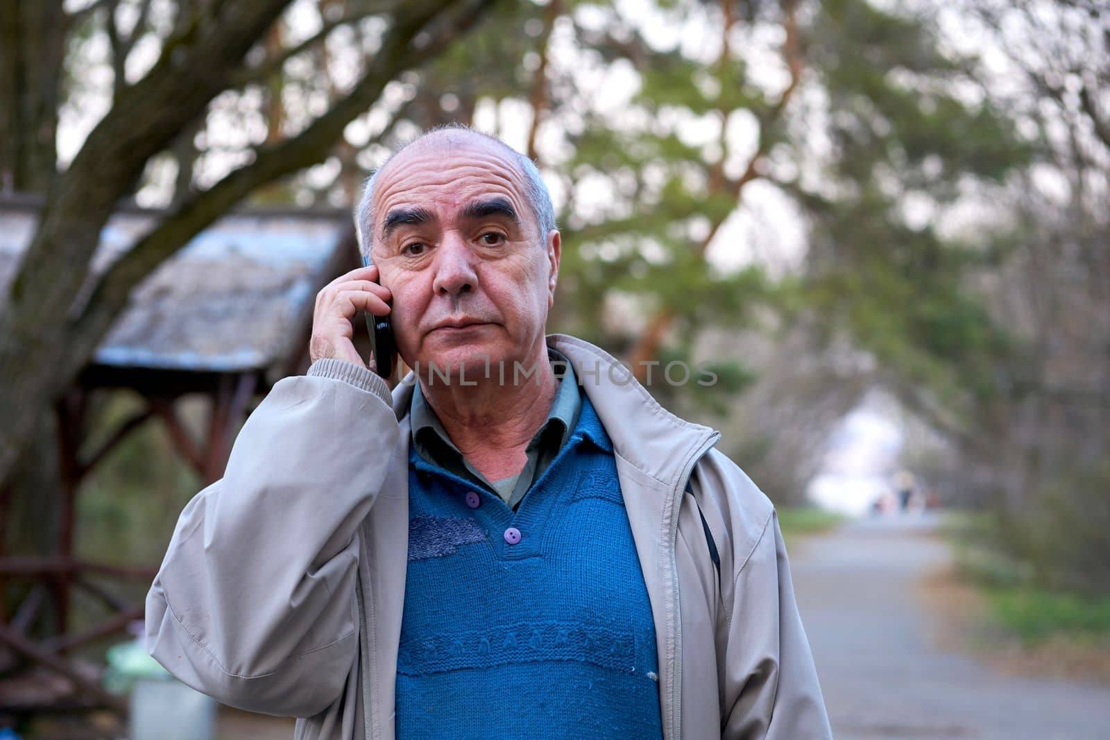 a human being regarded as an individual. Elderly retired man walking talking on the phone in a city park. High quality photo