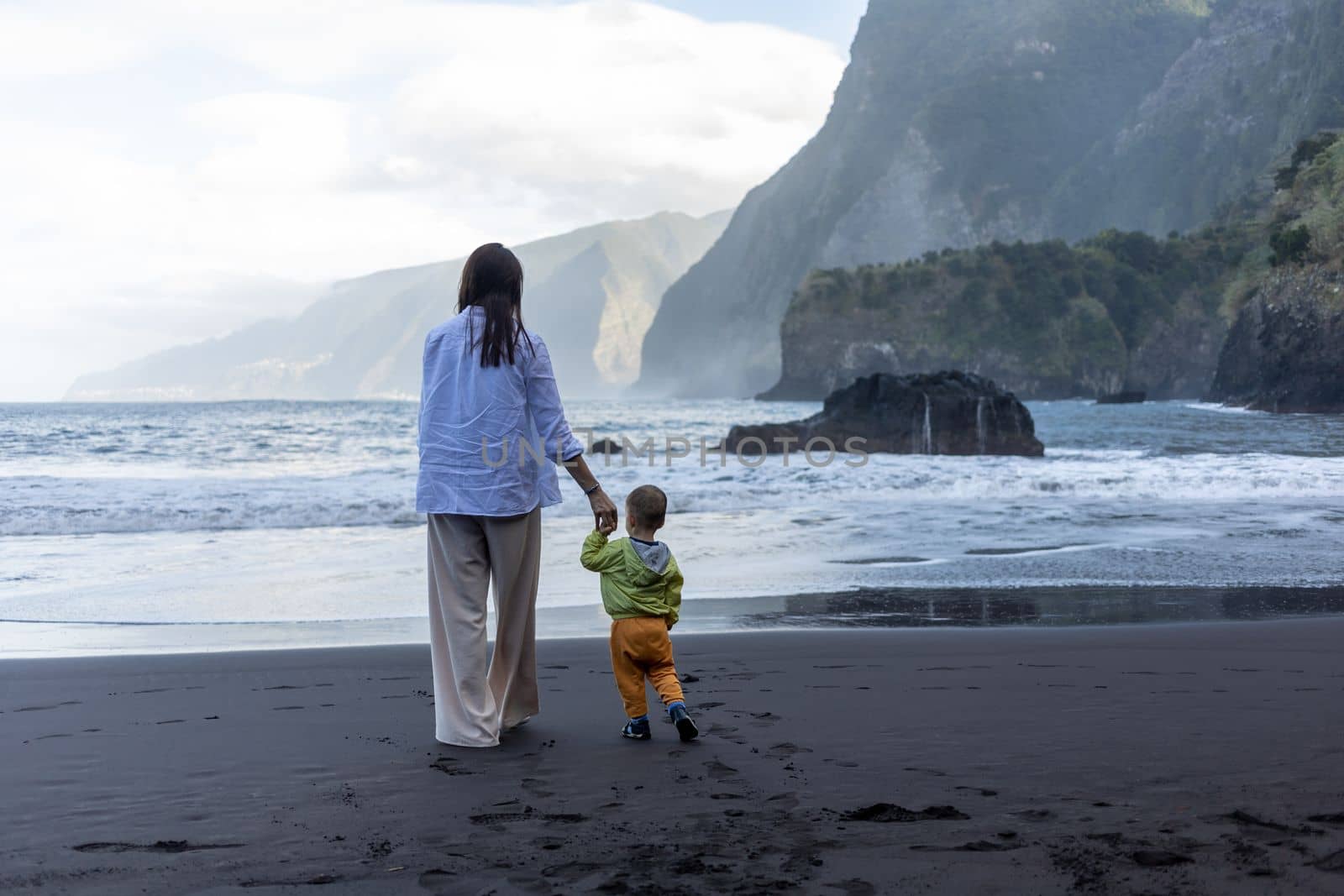 Mother and little child holding hands walking at sea side. High quality photo