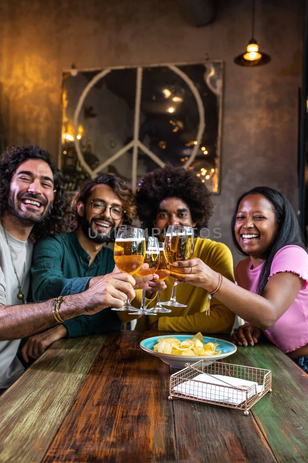 Happy multiracial friends in a bar looking at camera toasting with beer. Vertical image by Hoverstock