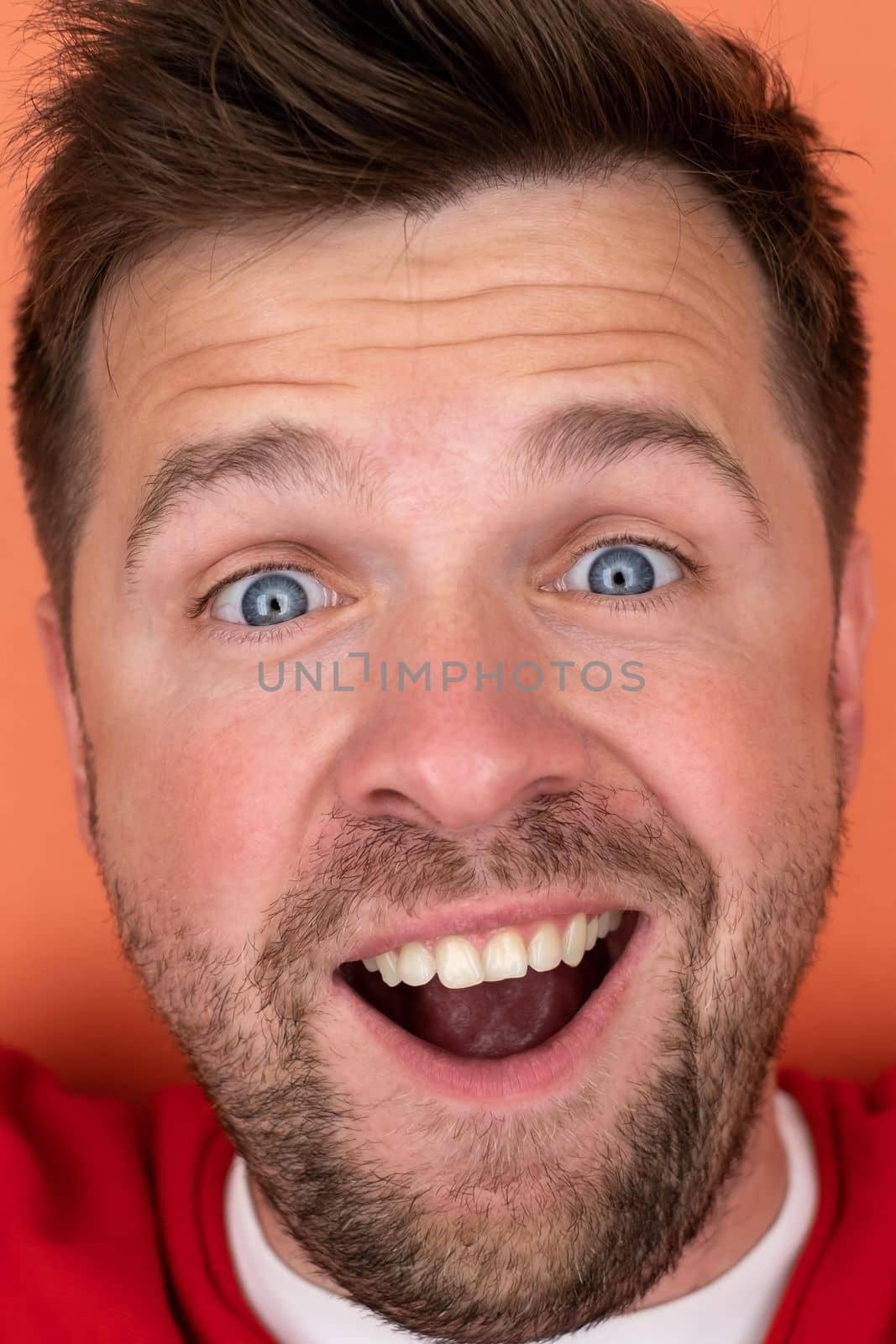 Handsome young man smiling while standing isolated on orange background.