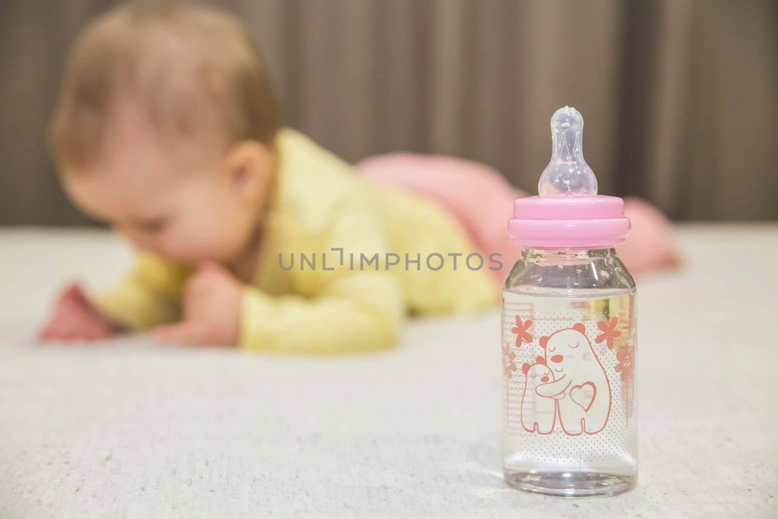 baby lies on the bed next to a bottle of water.