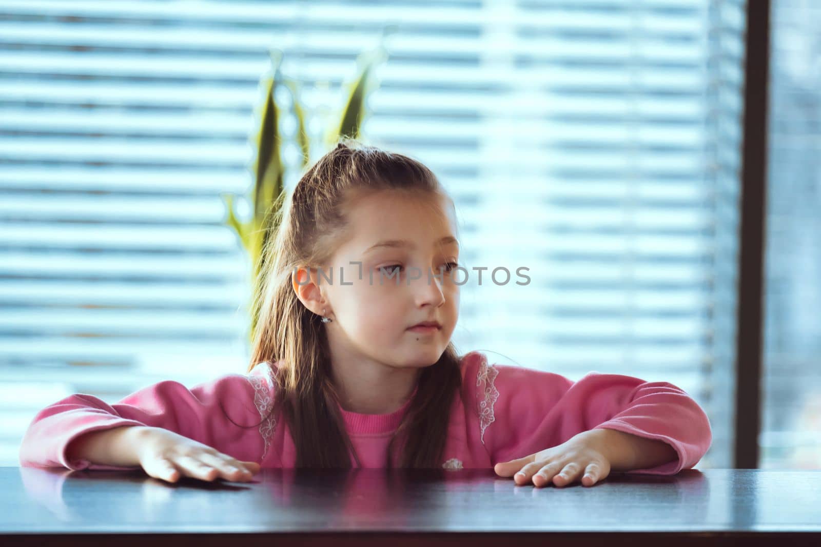 Child sitting on the table looking away to side. Portarit of a little girl in deep thought. by igor010