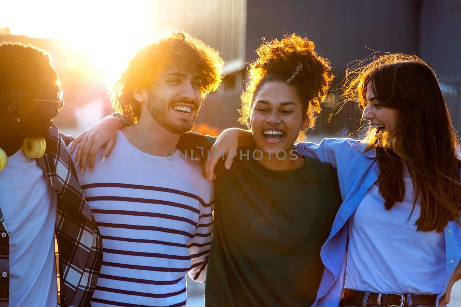 Back lit group of happy and smiling multiracial friends having fun together outdoors in the city during sunset. by Hoverstock