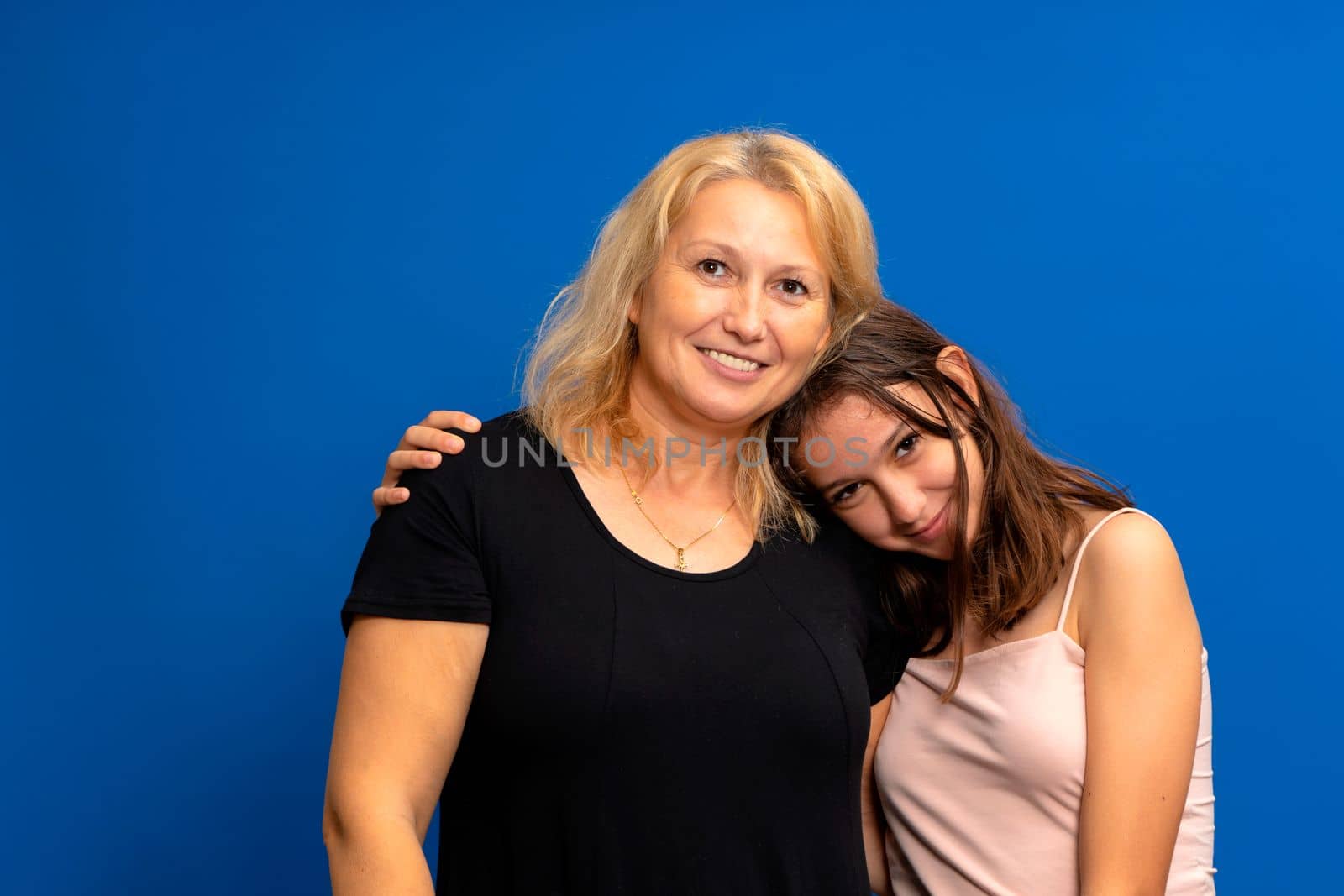 Headshot portrait of a smiling multiracial family of different female generations. Happy Caucasian mother in her 40s hugging the shoulders of a pretty Hispanic teenage daughter.