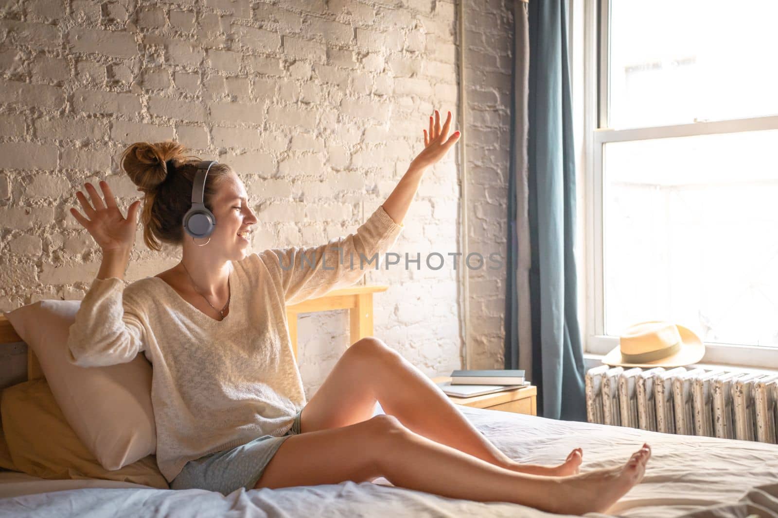 Young handsome woman listening to music with headphones in modern bedroom with brick wall. High quality photo