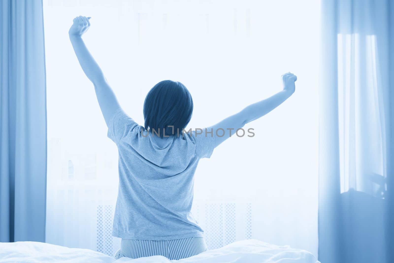 Woman stretching in bed after wake up, back view.