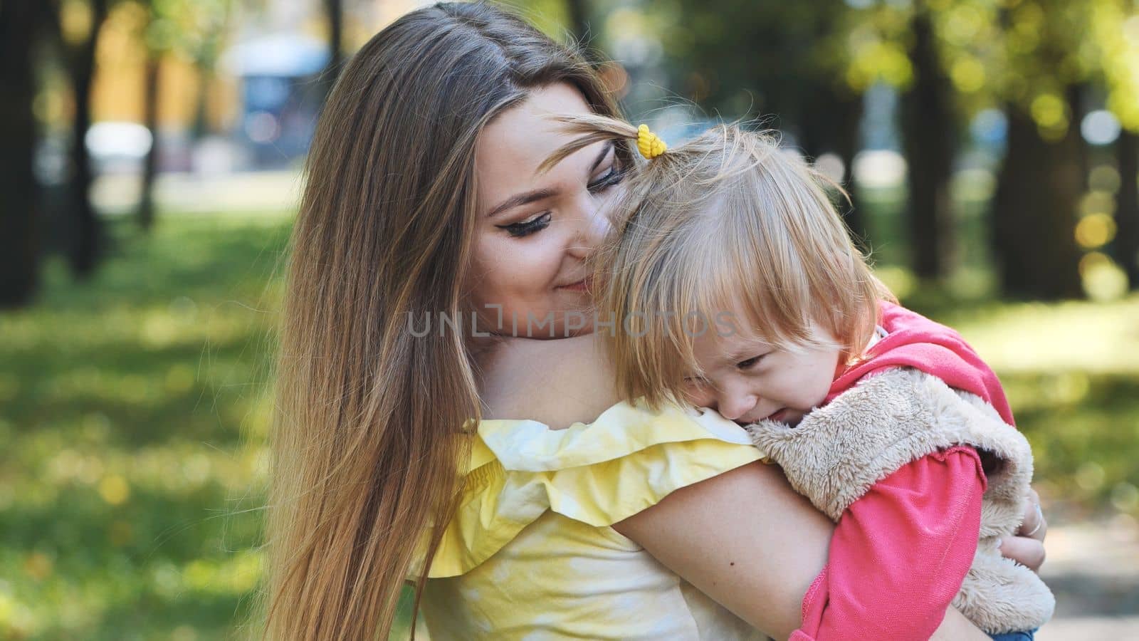 A mother hugs her young daughter in the park in the summer
