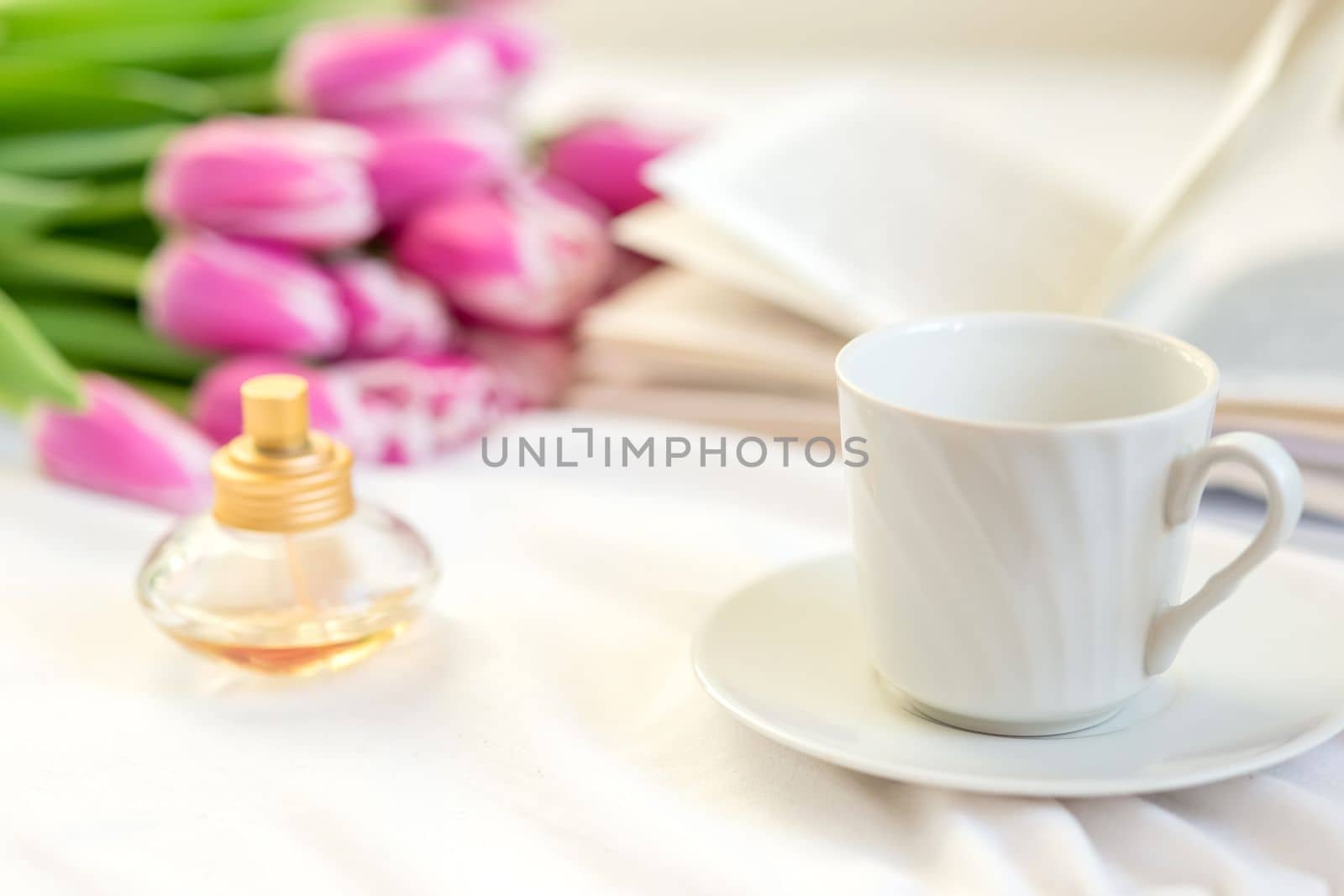 A still life with a white mug , a bottle of perfume, an open book and a bouquet of beautiful pink tulips by Zakharova