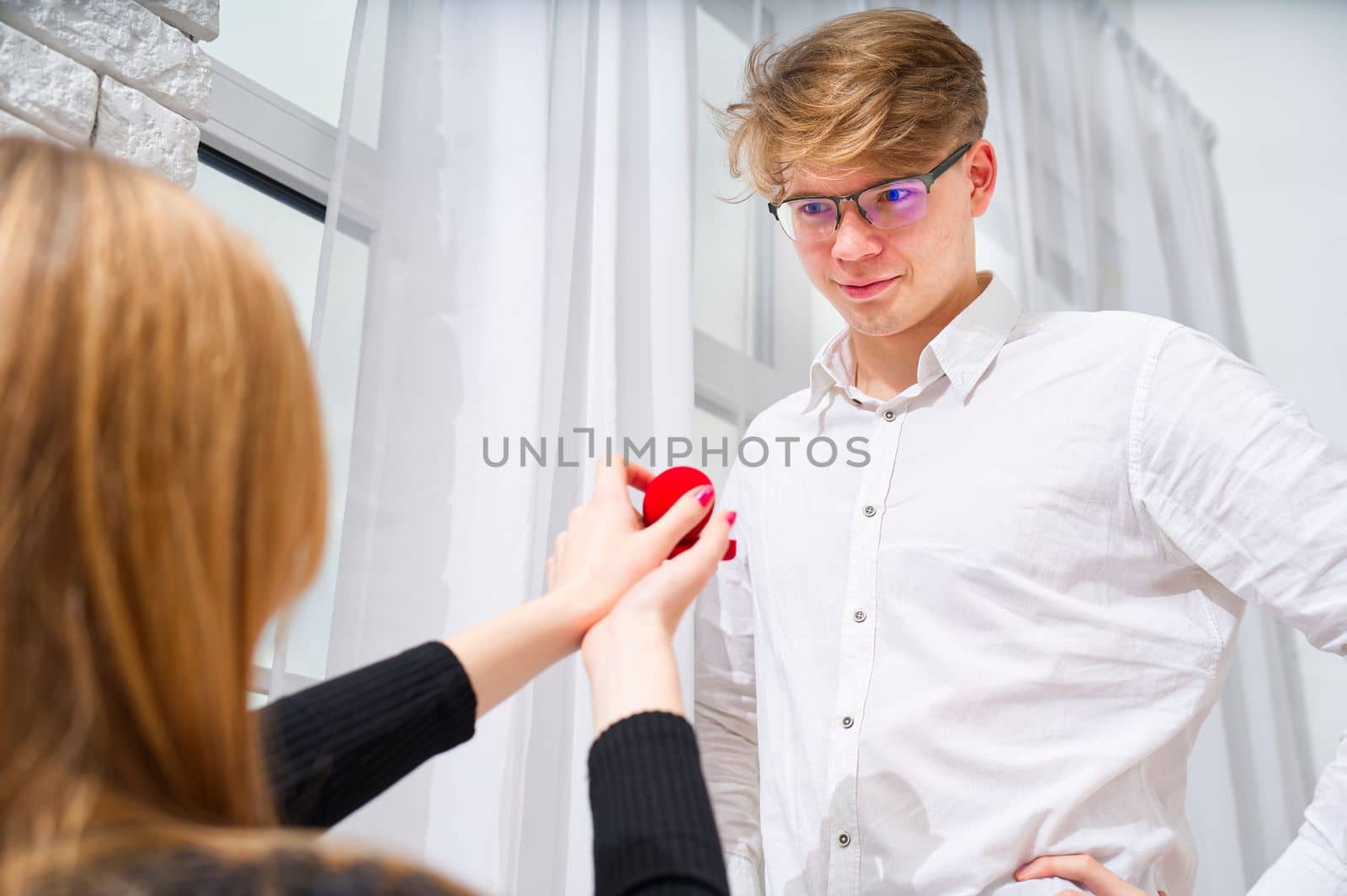 Embarrassing moment. Romantic concept. Young woman holding box with engagement ring, making marriage proposal to her boyfriend indoors, women psychology.