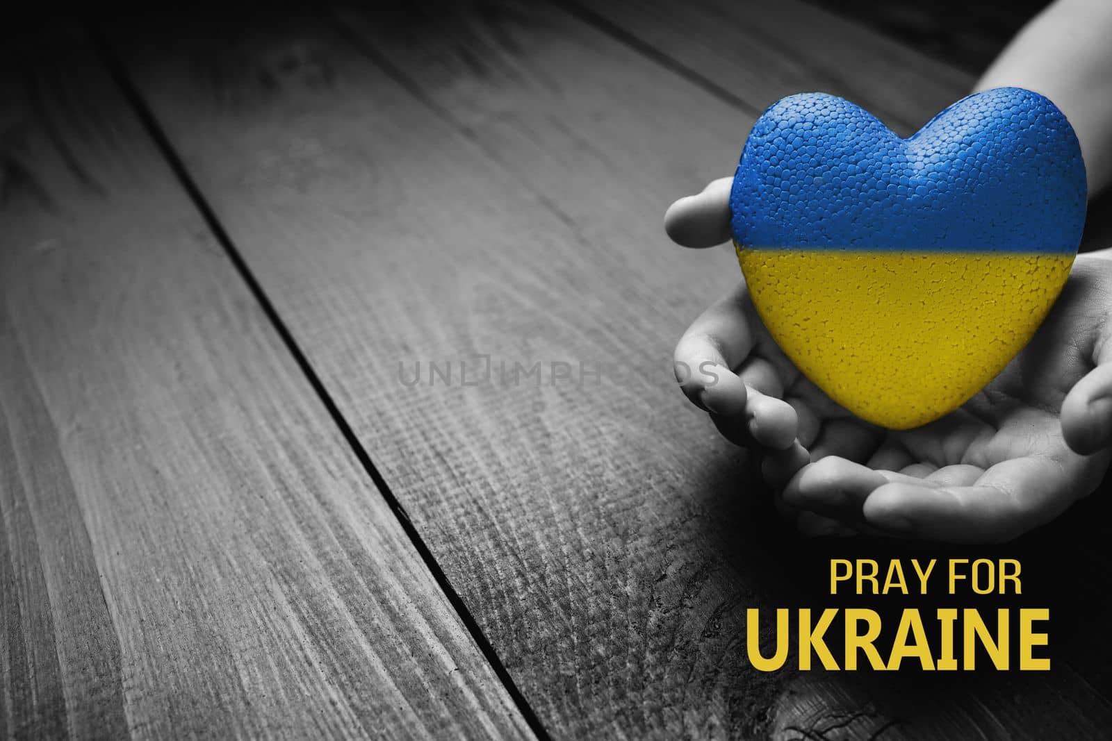hand holds yellow and blue heart on dark wooden background with words pray for Ukraine. needs help and support, truth will win