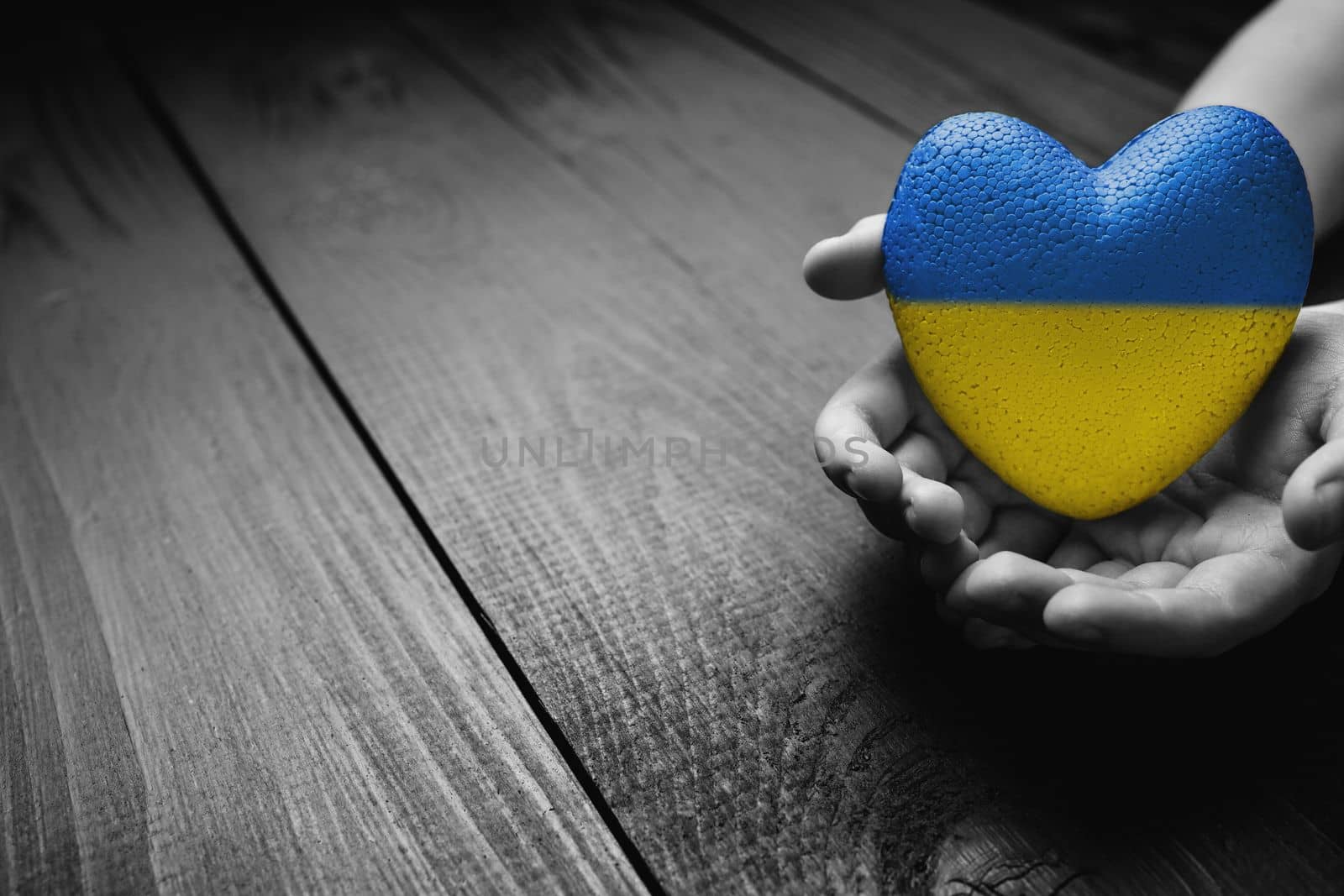 hand holds yellow and blue heart on dark wooden background. black and white color. concept needs help and support, truth will win