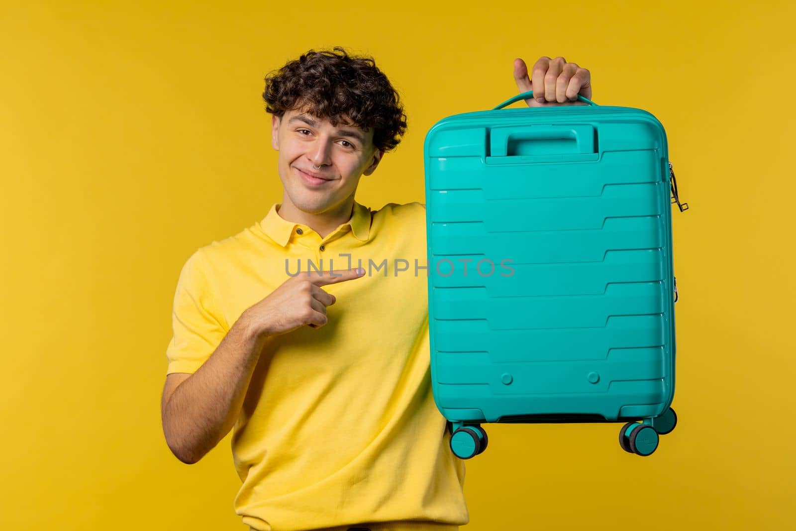 Young man with carry-on suitcase on yellow background. Teenager traveling with blue luggage bag for airplane hand baggage. Summer travel, vacation concept. High quality photo