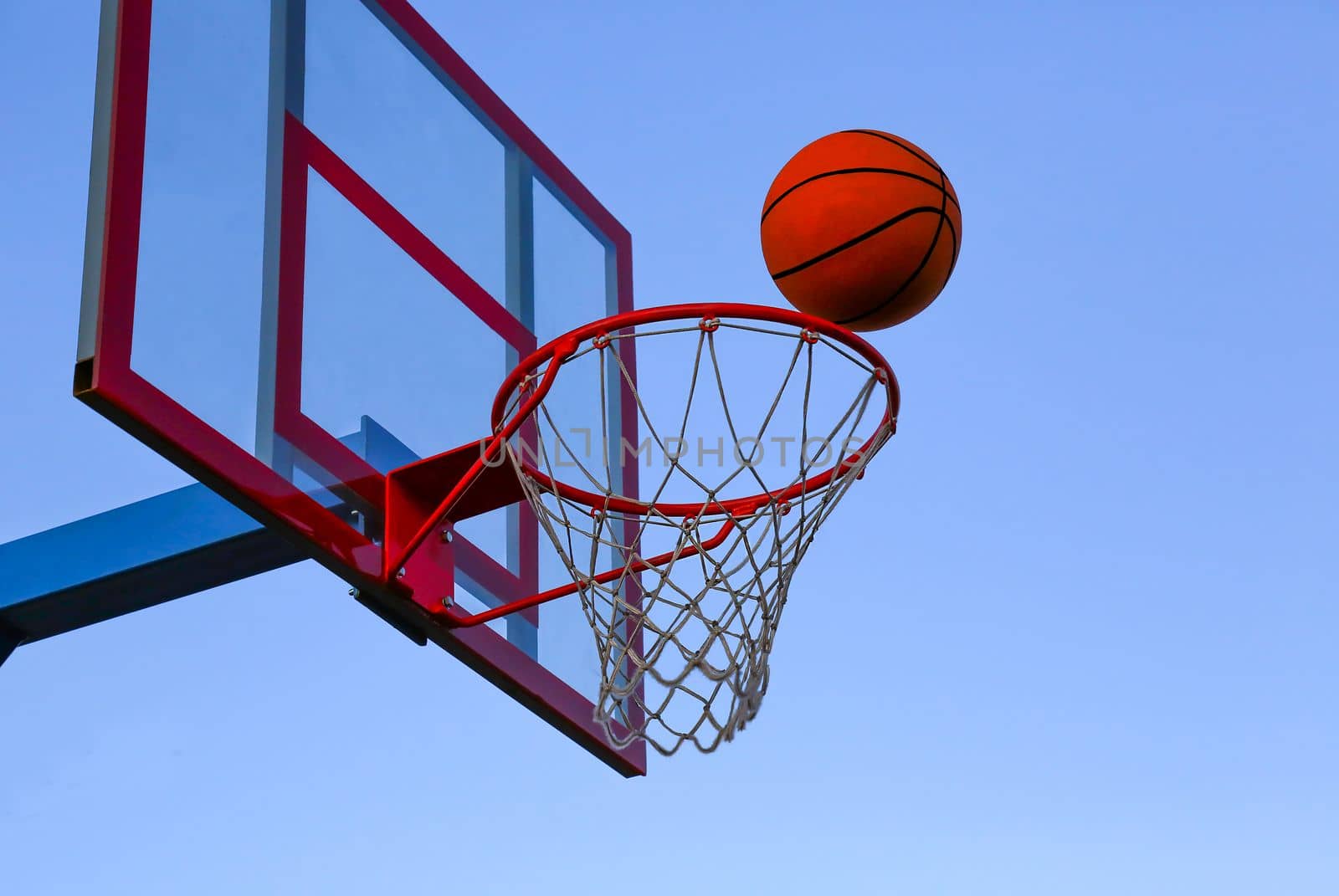 A basketball ball flies into a basket on an open basketball court. Basketball against the sky.