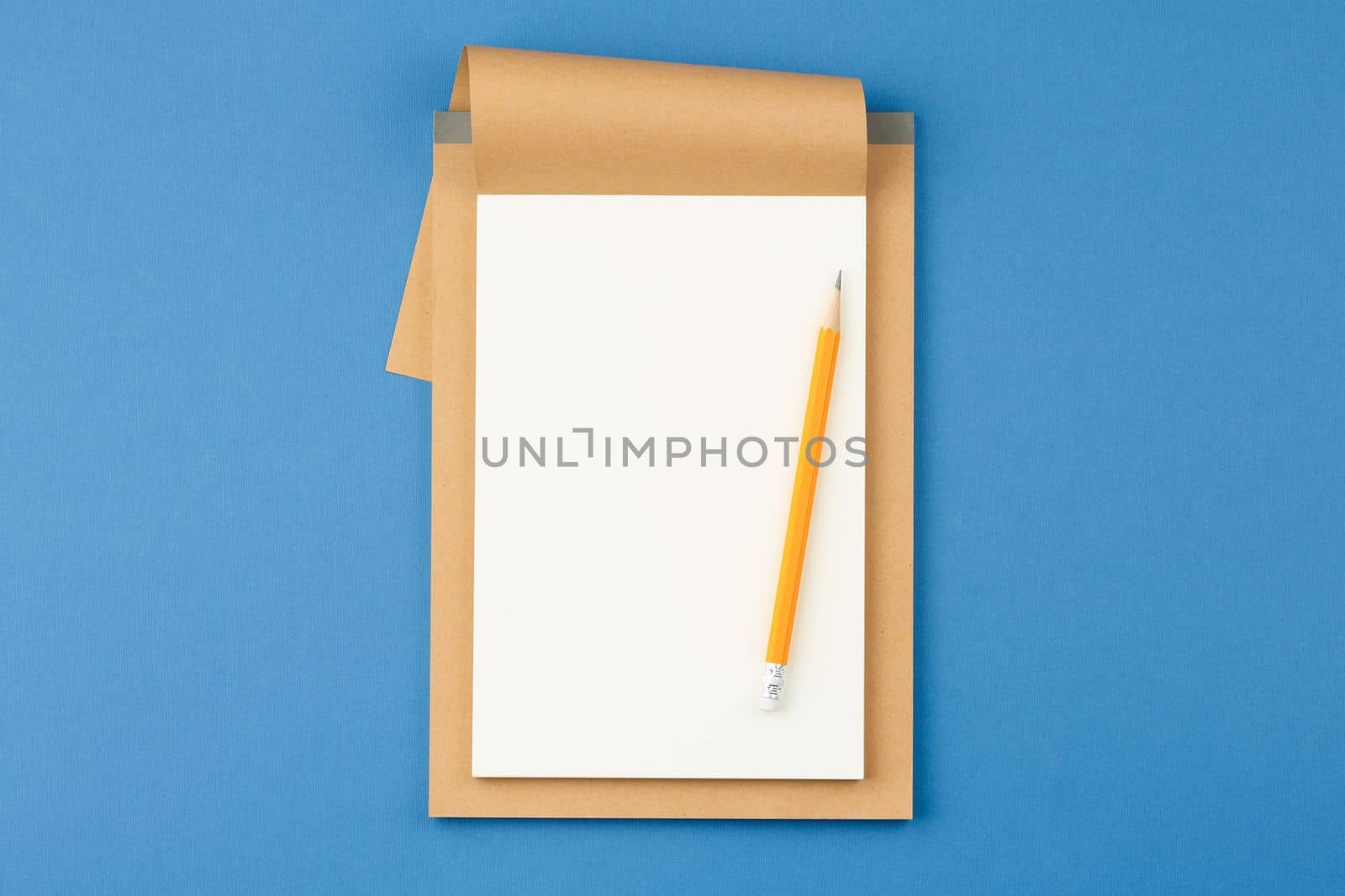 Open notebook with white blank sheet and pencil on blue isolated background. Top view.