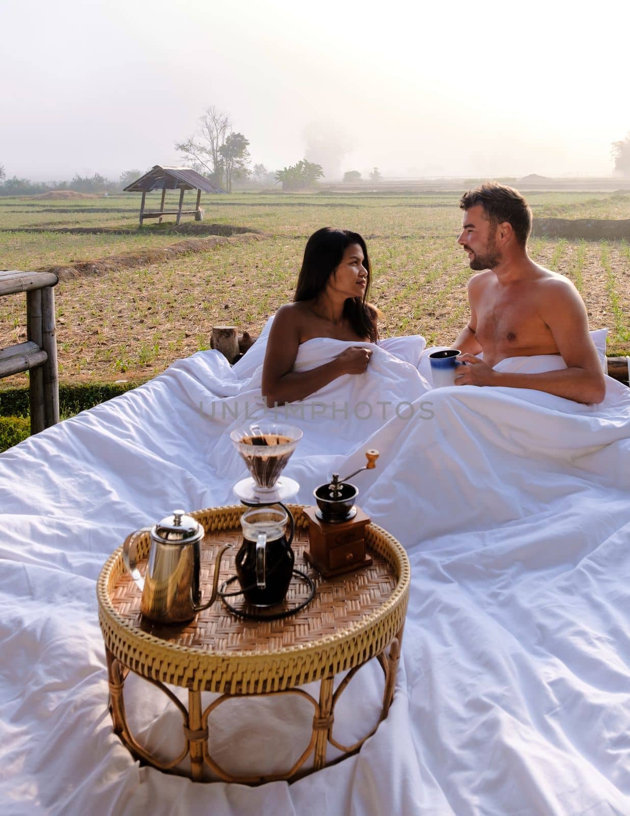 A couple of men and women at a cottage homestay in an outdoor bed in Northern Thailand Nan Province, couple waking up during sunrise in the rice fields in the morning drinking coffee outside