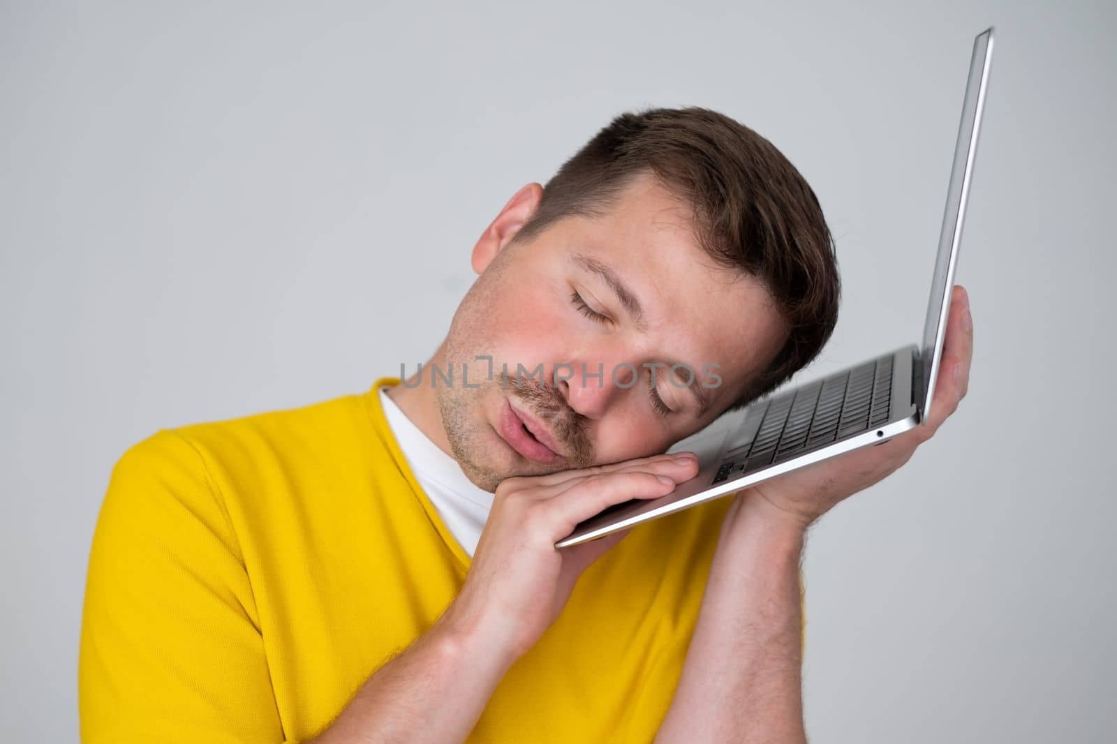 Tired caucasian man sleeping on a laptop having a nap time. Studio shot