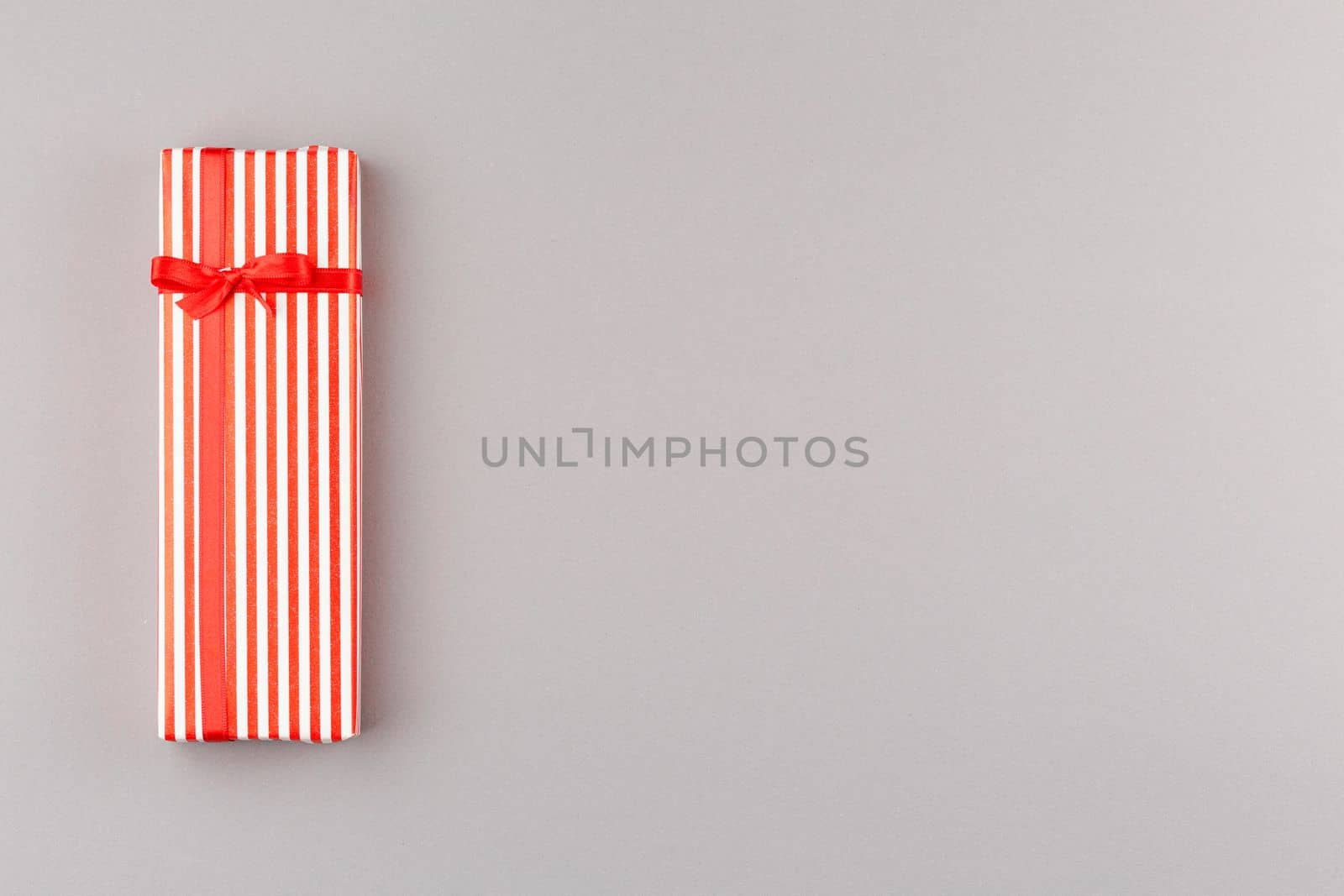 Present in striped paper with red satin bow on gray isolated background. Flat lay. Gift box with satin red bow. Top view.