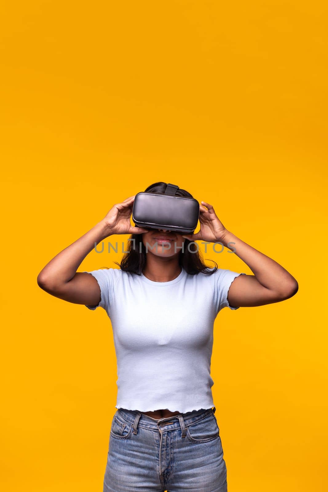 Young woman wearing VR headset on yellow background. Vertical portrait of Asian female wearing virtual reality goggles. by Hoverstock