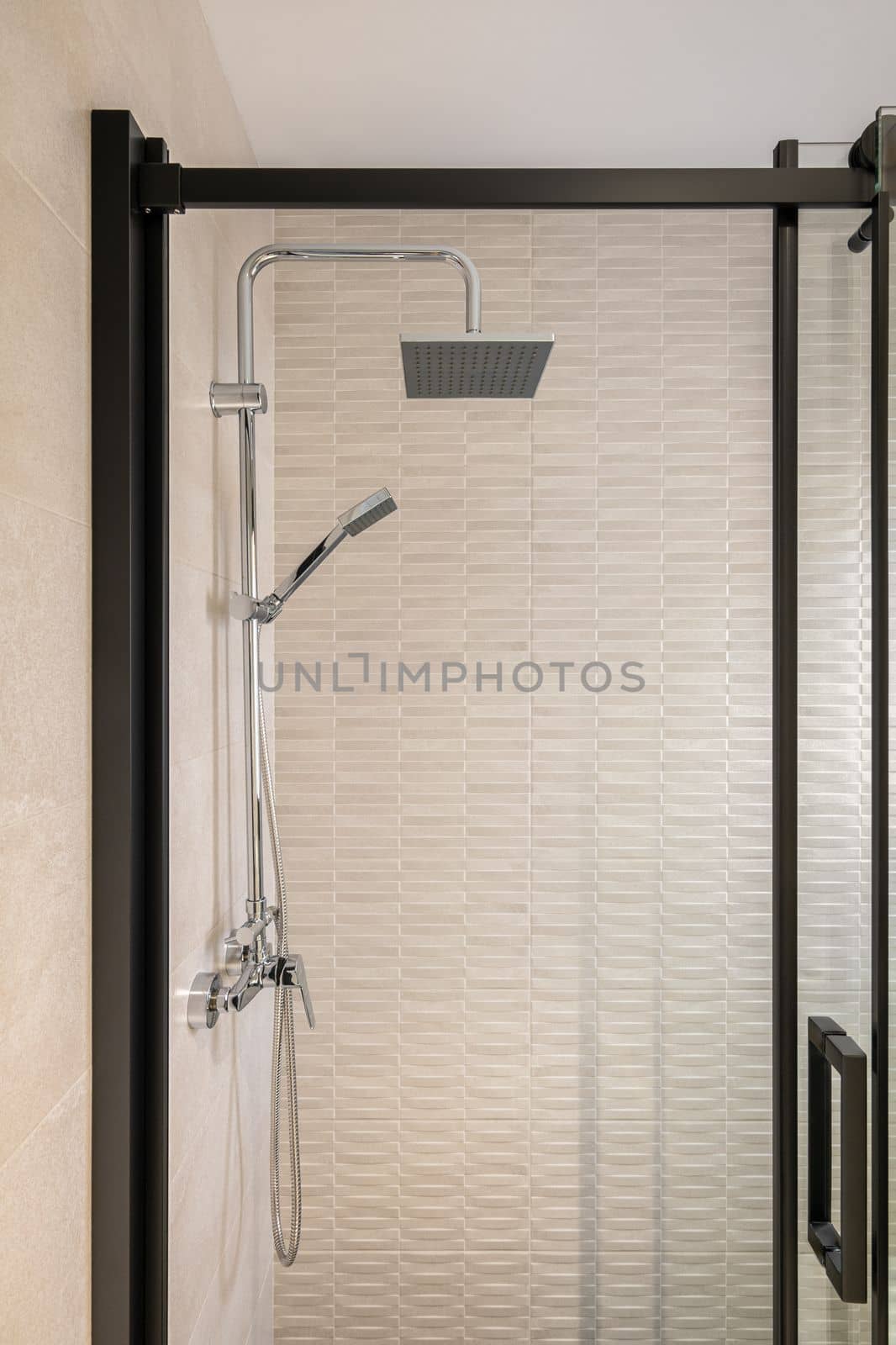 Modern tiled bathroom with rain head, hand held shower and glass door with black framing. by apavlin