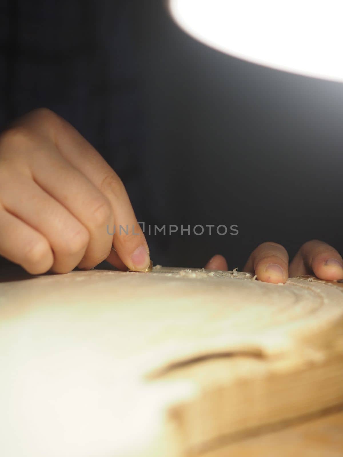 artisan working on raw wood violin plate with finger plane on the bench
