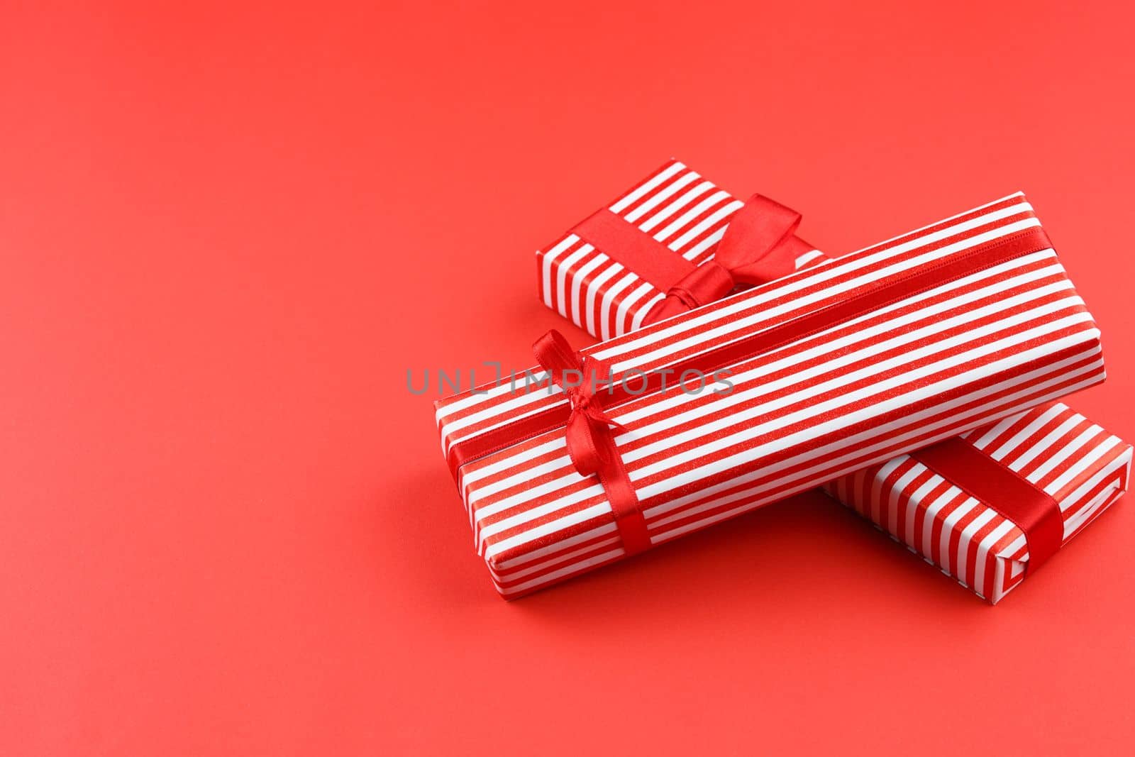 Gifts in striped wrapping paper with red bow on red isolated background. Present boxes