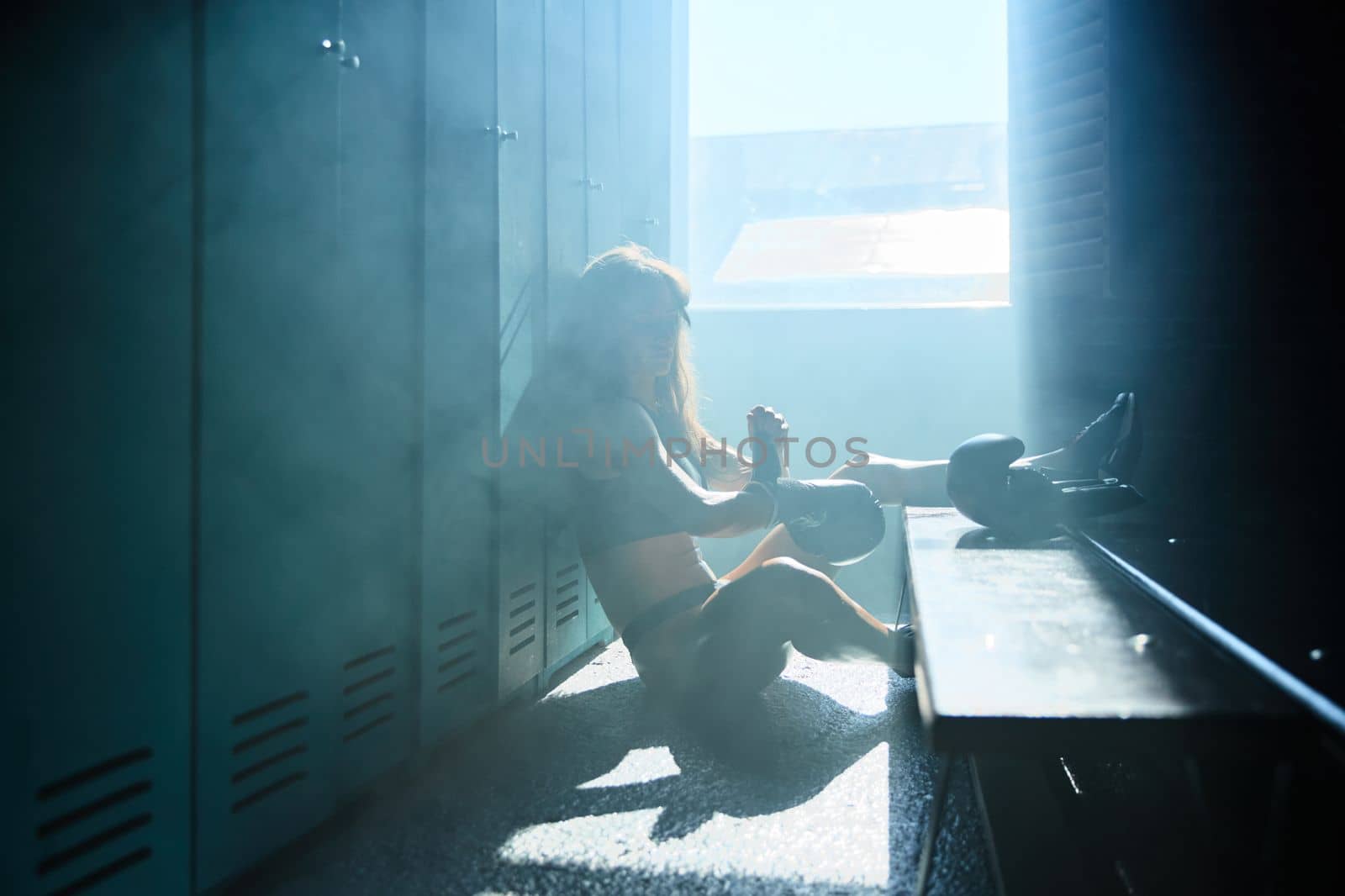 Young girl of an athletic build in the locker room of a sports club wears boxing gloves, a girl is dressed in sports black underwear, sun rays from window, sneakers by vladimirdrozdin