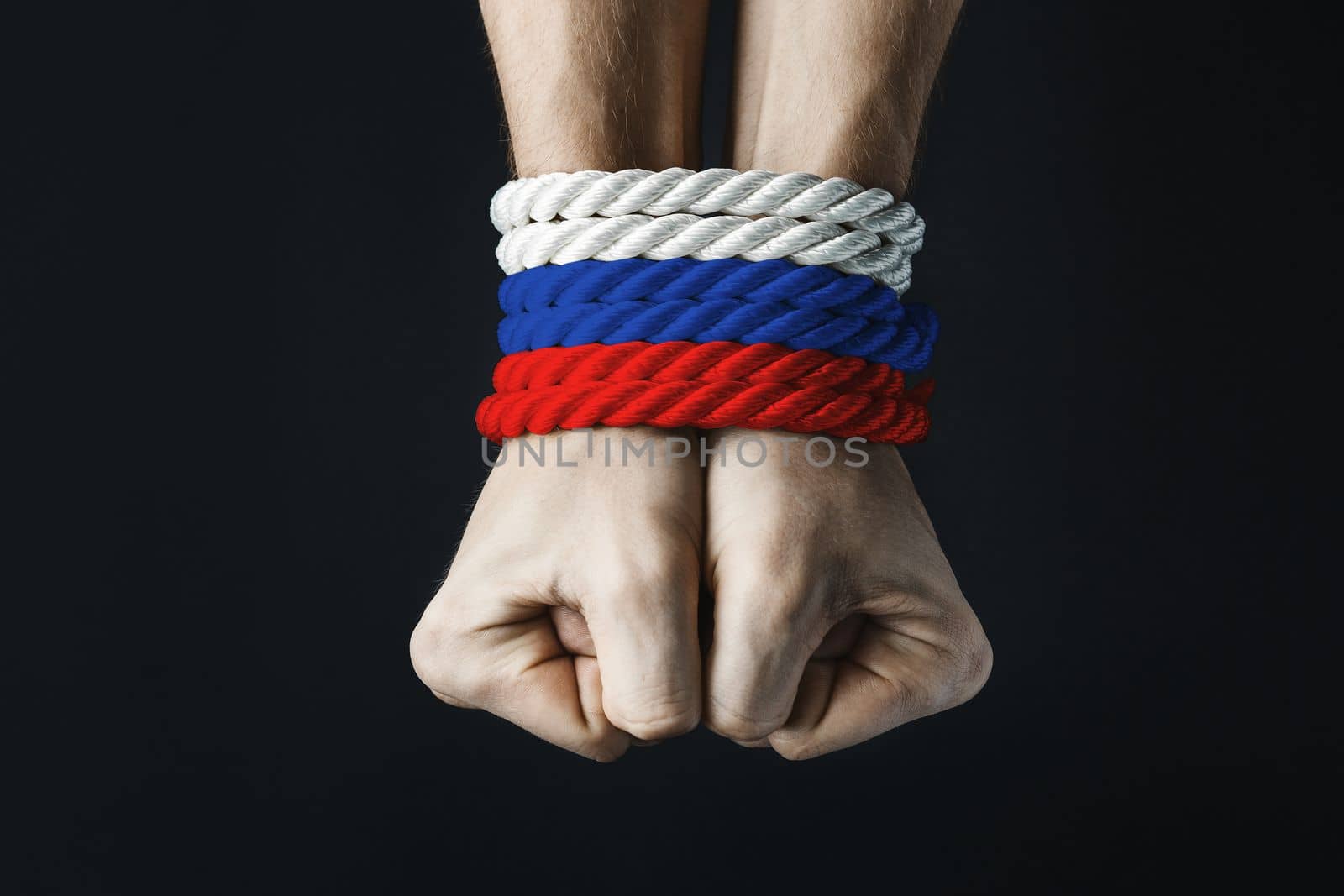 tightly tied mans hands with russian tricolor red blue white rope on dark background, violence and kidnapping.. concept needs help and support, truth will win