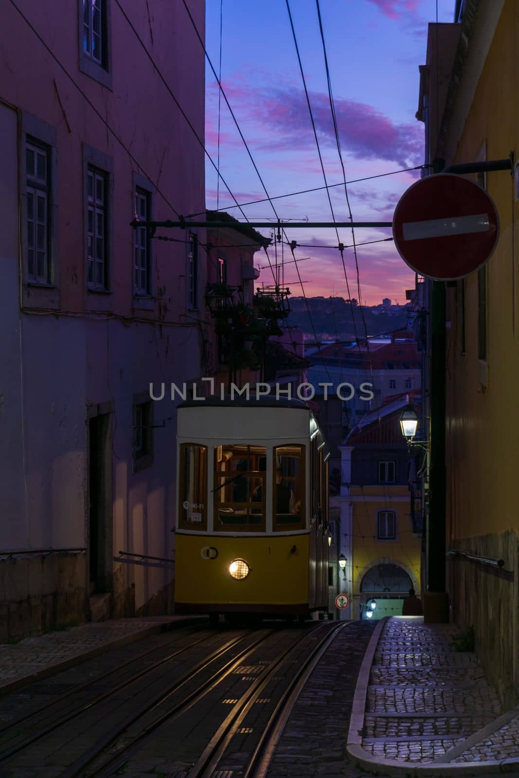 Antique yellow cable car on a narrow Portuguese street at sunset cityscape