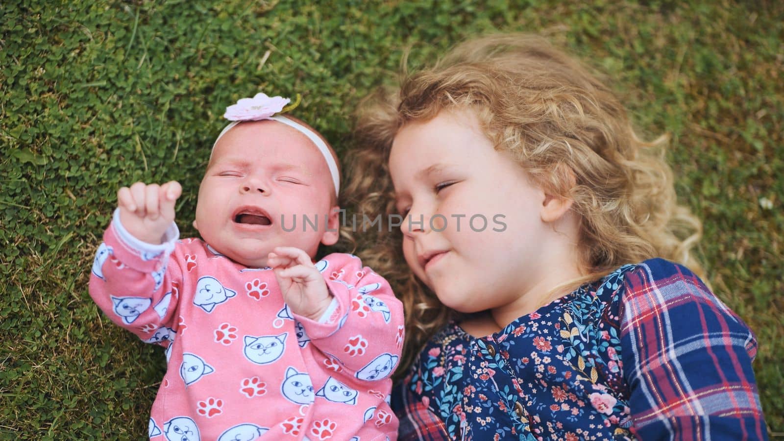 A little girl kisses her baby sister in the garden on the grass