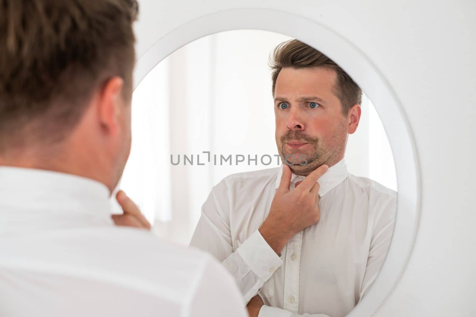 young caucasian man with a double chin examing his reflection in mirror