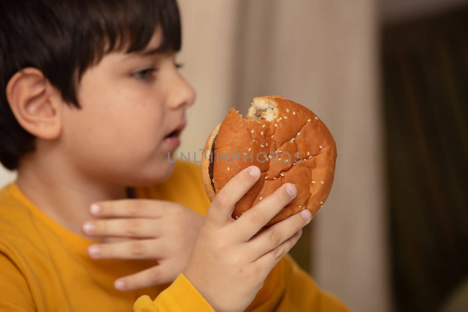 Cute healthy preschool kid boy eats hamburger sitting in school or nursery cafe. by senkaya