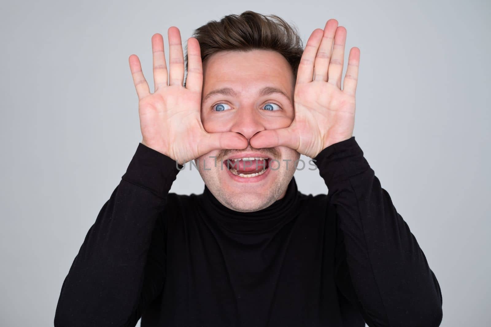 Caucasian man showing big mustache with hands. Studio shot