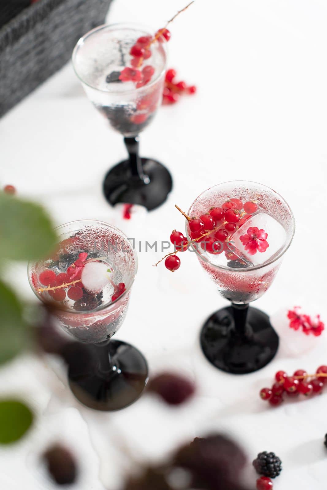 transparent gin and tonic with ice and fresh red currants and blackberries in beautiful crystal glasses against the background of a vase of flowers. High quality photo