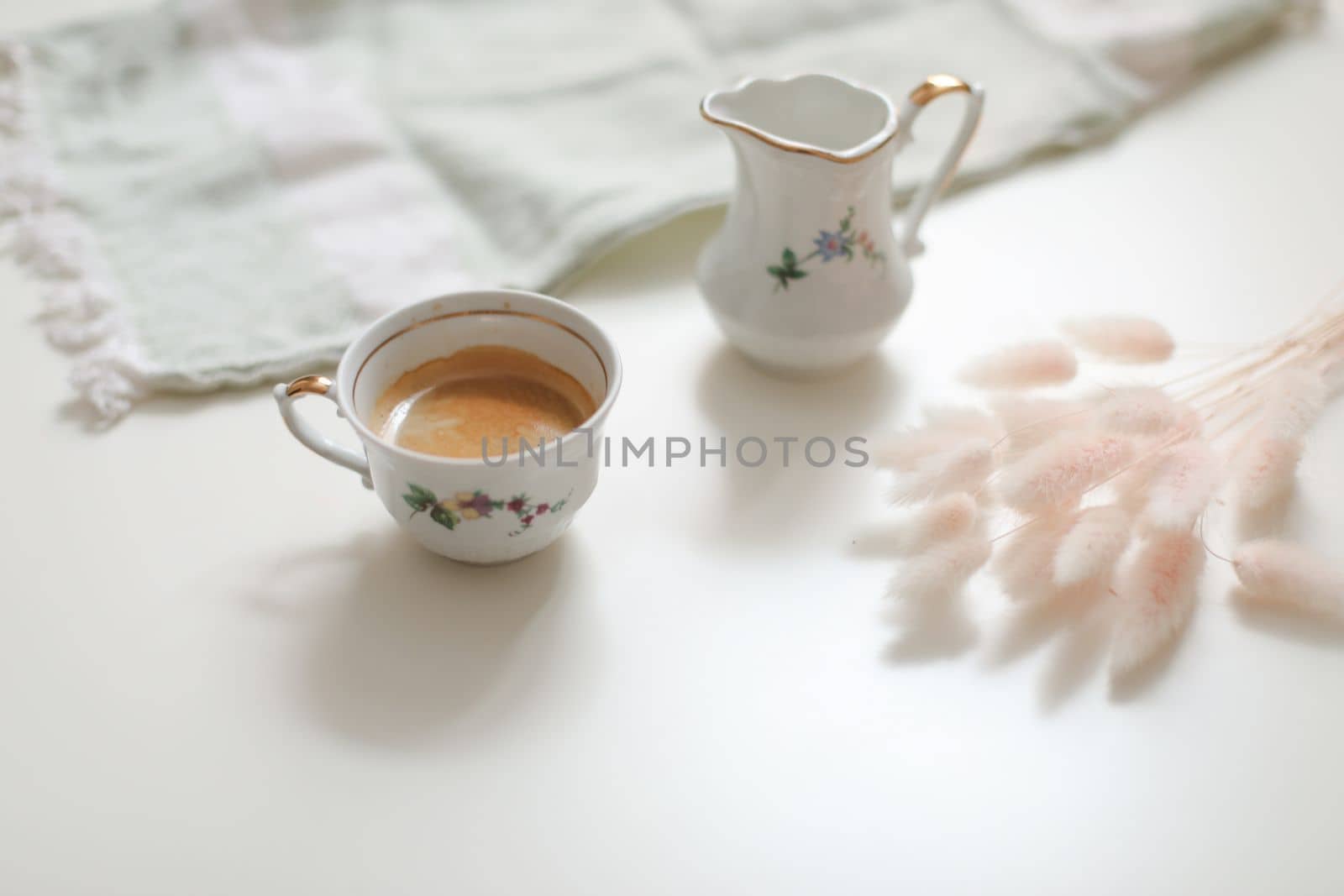 cup with coffee and milk jug on a white wooden background, closeup. Energy breakfast, morning routine concept by paralisart