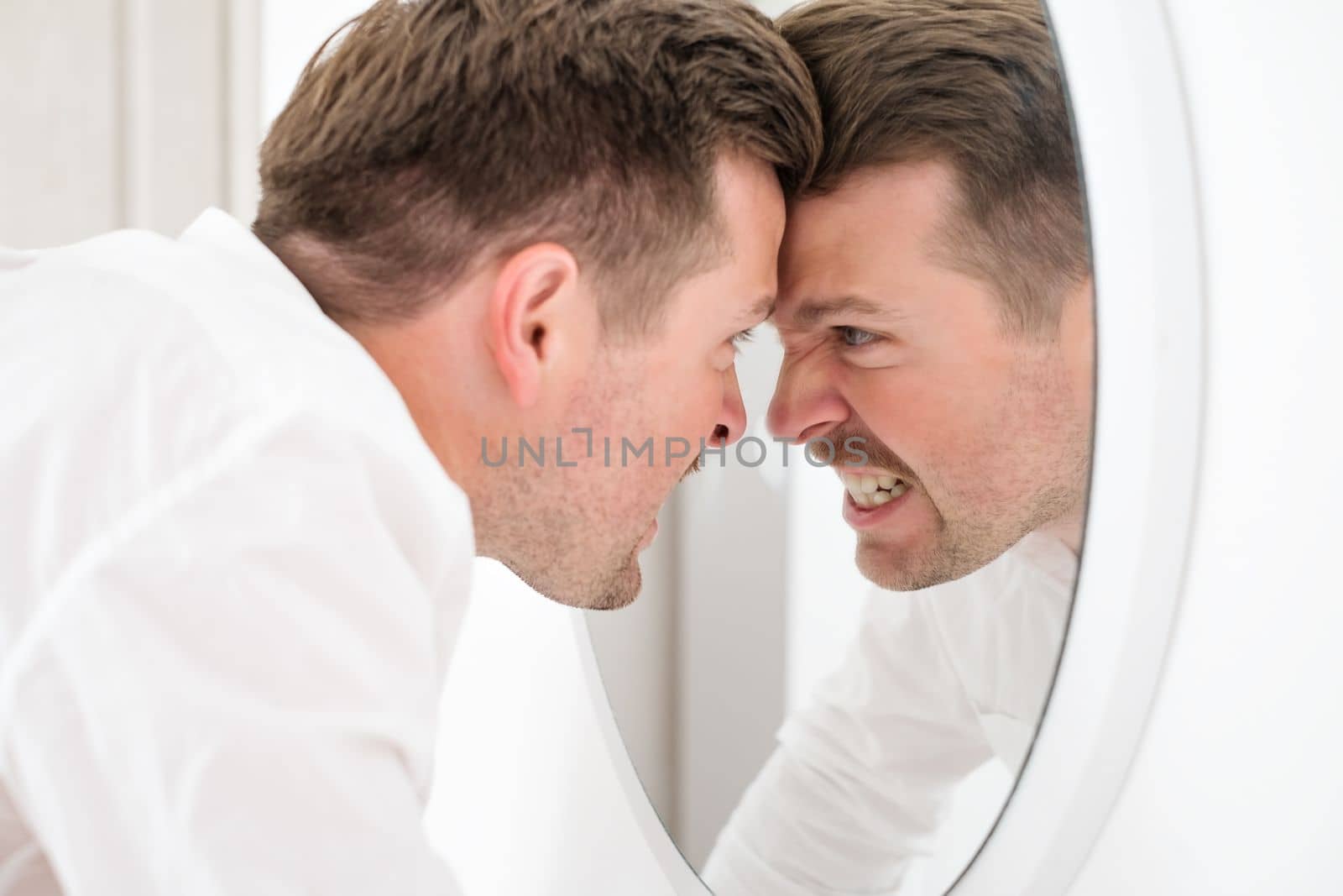 Caucasian man being angry on himself screaming on his reflection on the mirror. Self harm and abuse concept.