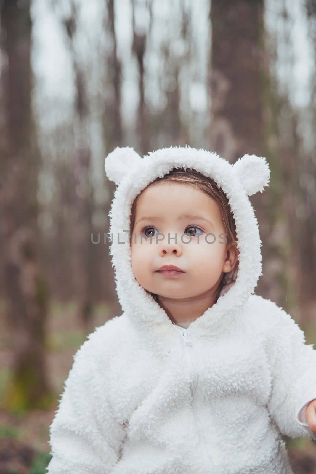 Adorable baby in a bear costume in the forest by a fallen tree.