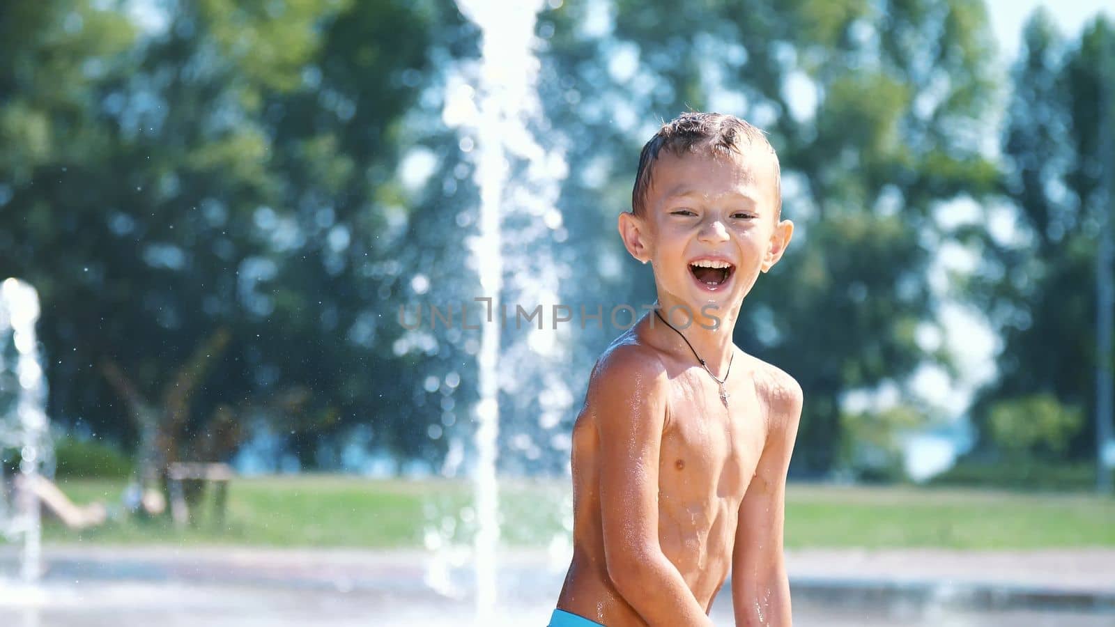 excited boy of seven years having fun between water jets, in fountain, run around, sprinkle, have fun, have fun, on a hot summer day. Summer in the city. Slow motion. High quality photo