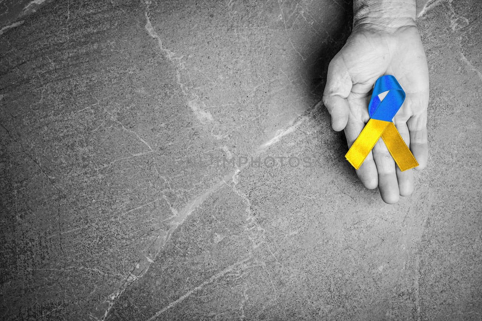male hand with yellow and blue ribbon on marble background black and white color. concept needs help and support, truth will win