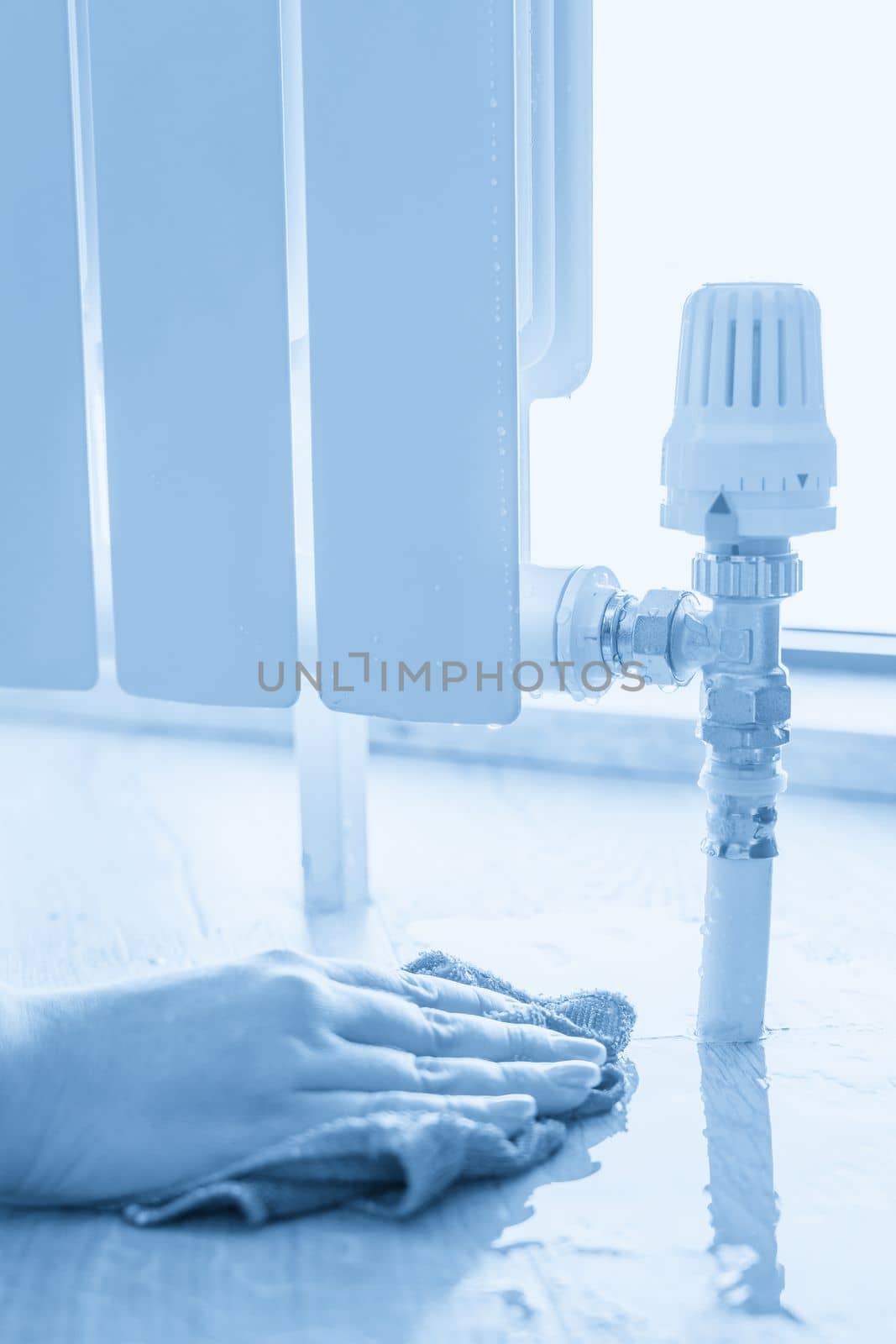 Female hand with rag cleaning water from heating radiator leak by Mariakray